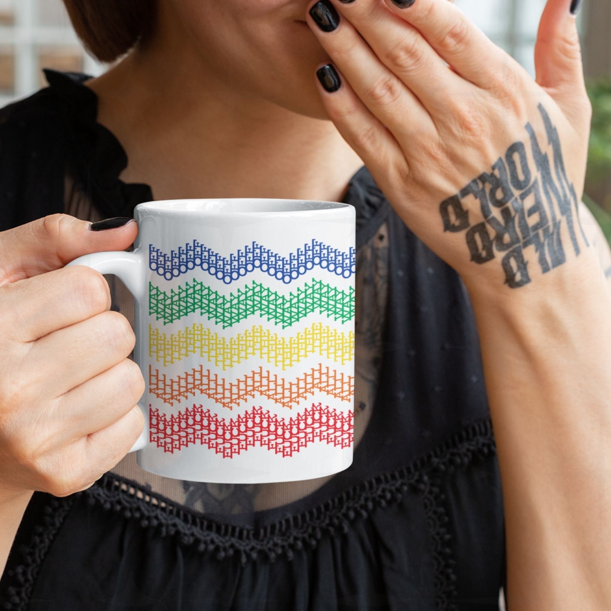 Woman with black nail polish and hand tattoo holding rainbow stripes hidden profanity chevron mug, covering smile while reading the hidden text