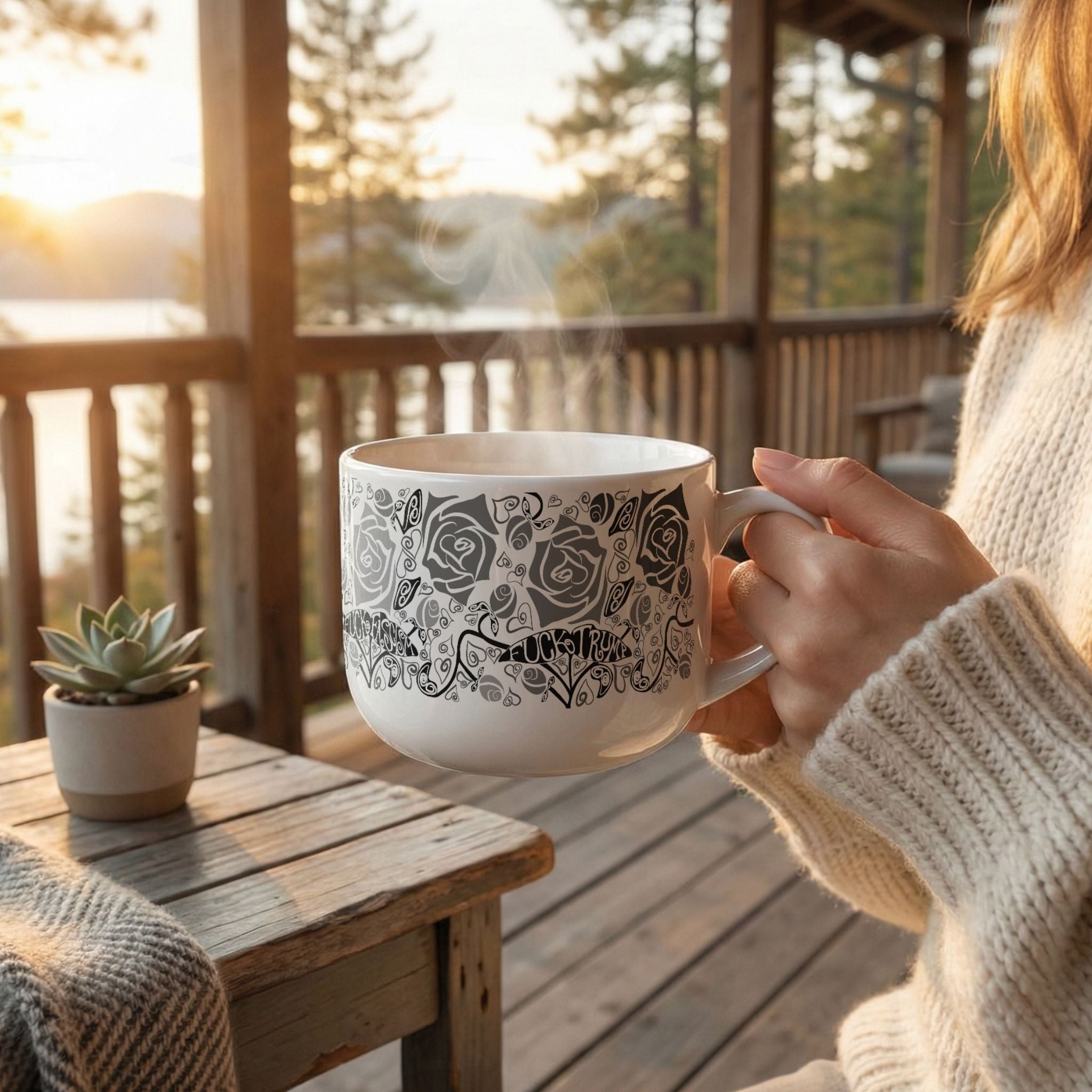 Woman holding hidden profanity latte mug on cabin porch at sunrise, monochrome rose and hand-lettered protest banner design visible on white ceramic