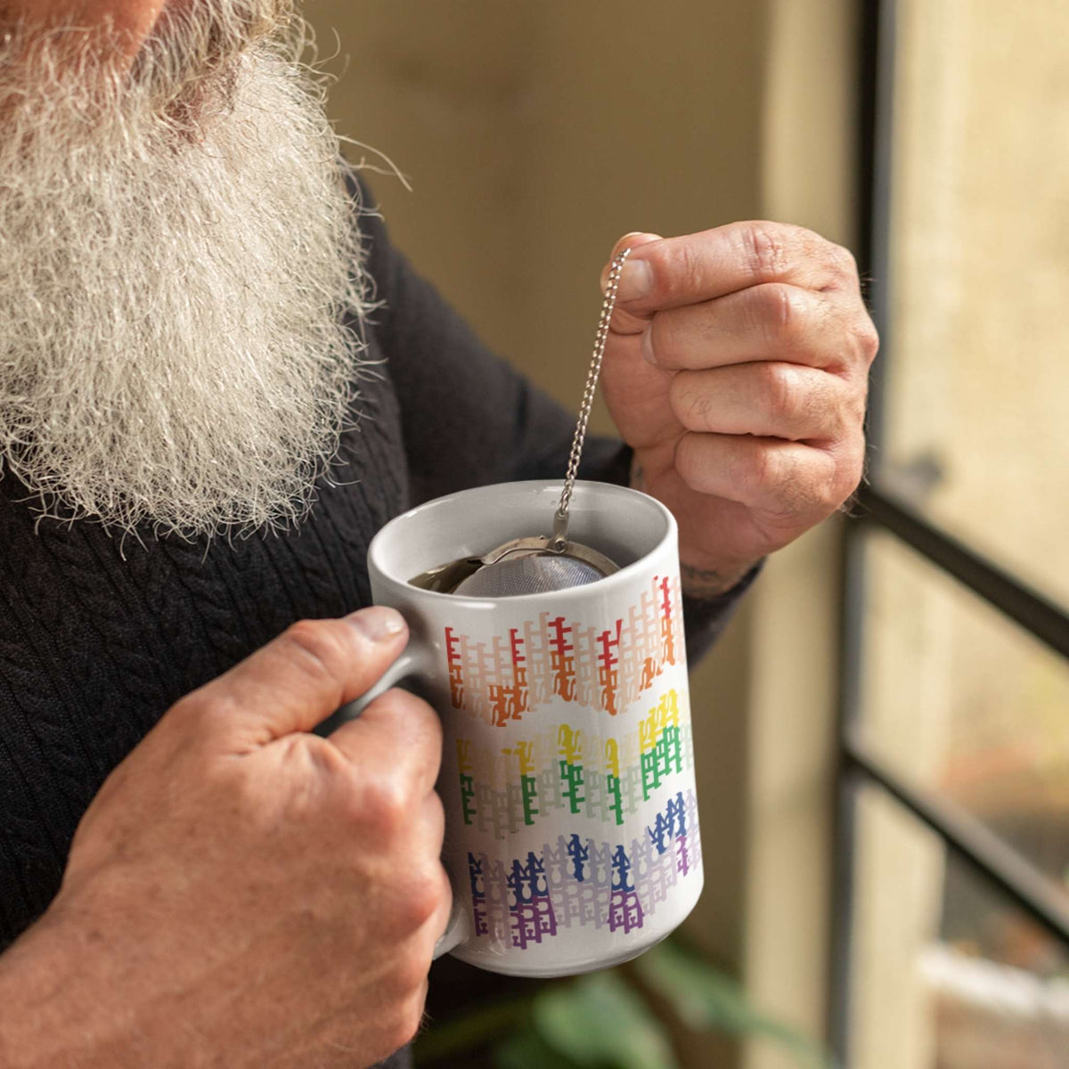 Bearded person in dark sweater steeping tea in 15oz hidden profanity mug with rainbow typographic chevron pattern