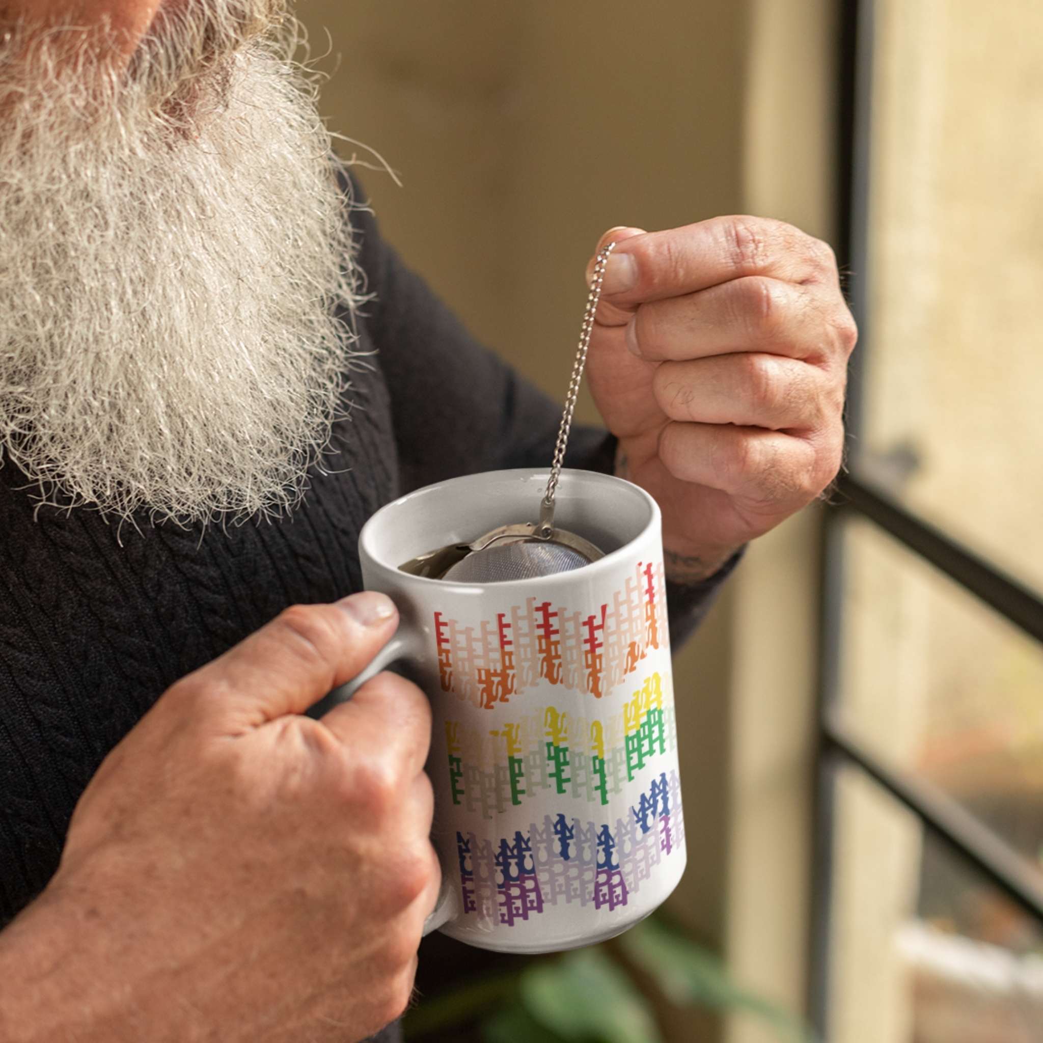 Bearded person in dark sweater steeping tea in 15oz hidden profanity mug with rainbow typographic chevron pattern