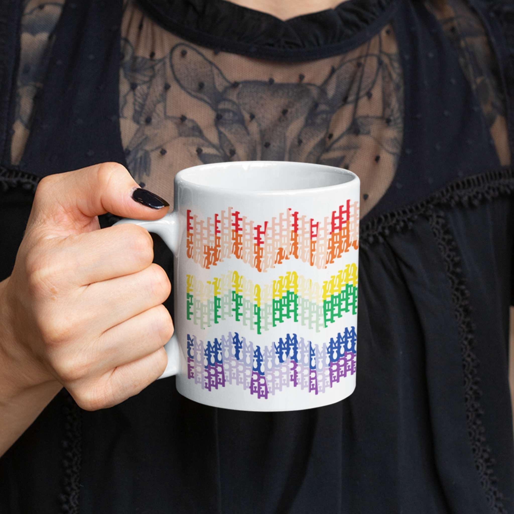 Woman in black lace top holding 11oz hidden profanity mug with rainbow chevron pattern, dark nail polish