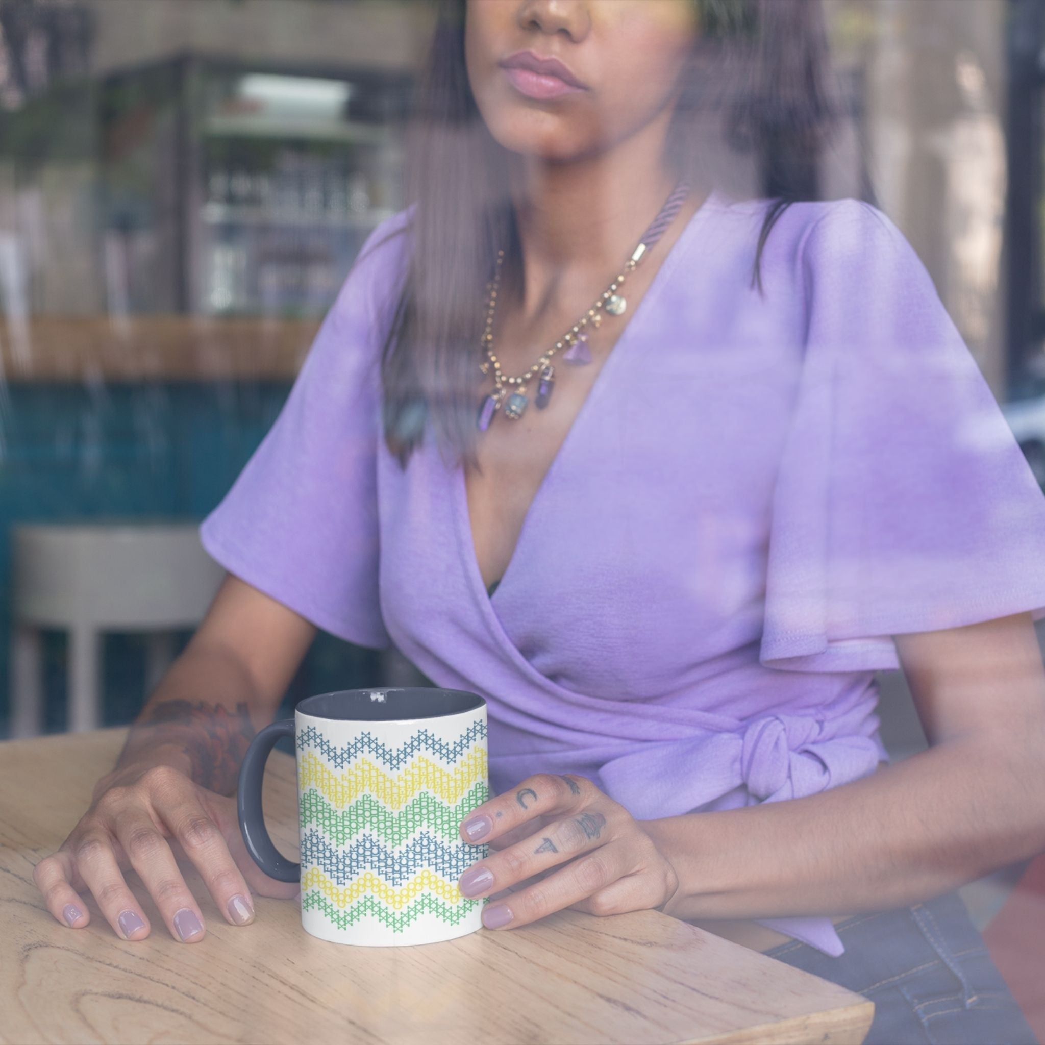 Woman sitting at cafe table with hidden message cross stitch mug in bright stripe navy accent colorway, shot through window