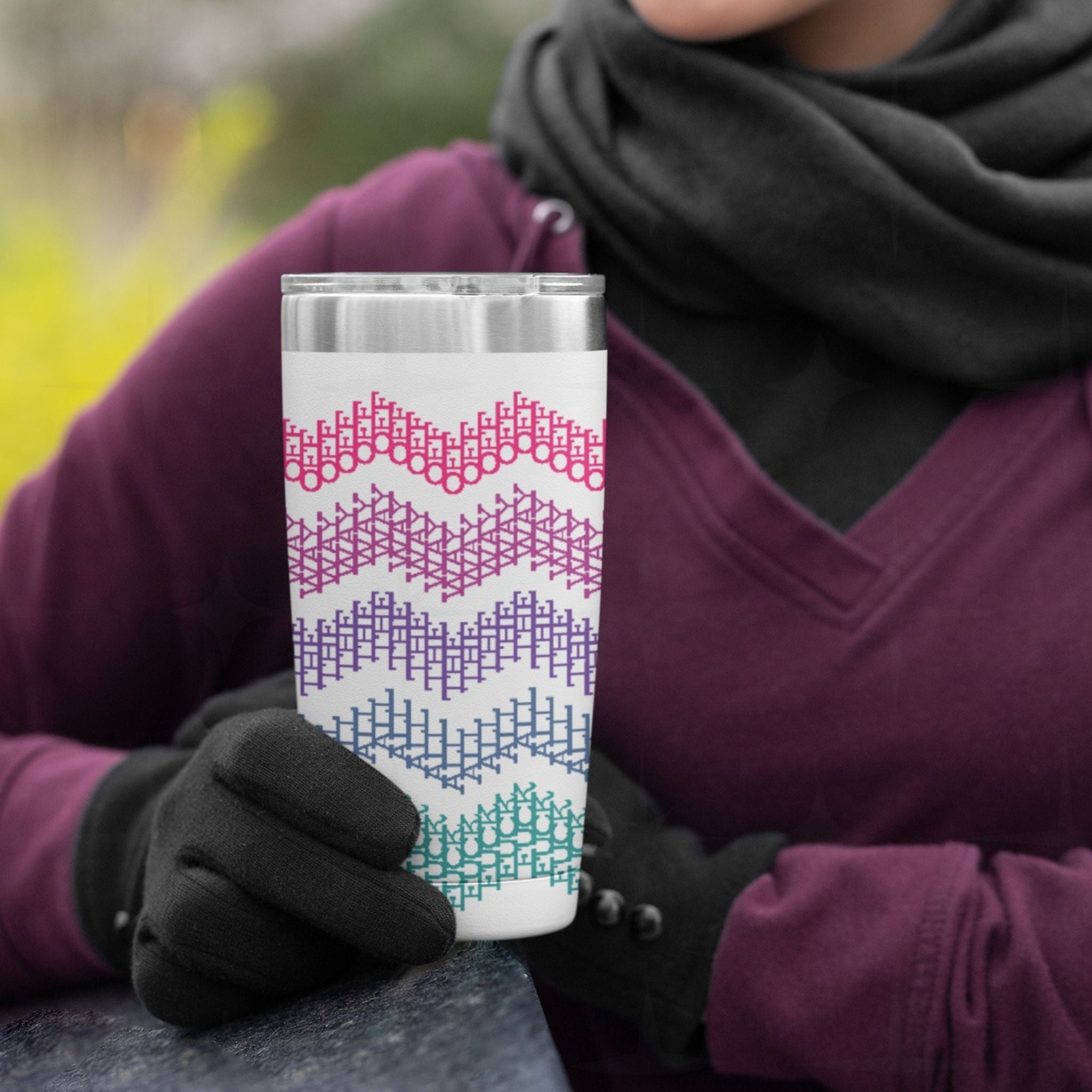 Person in plum hoodie and gloves holding bright stripe hidden profanity tumbler outdoors in cold weather