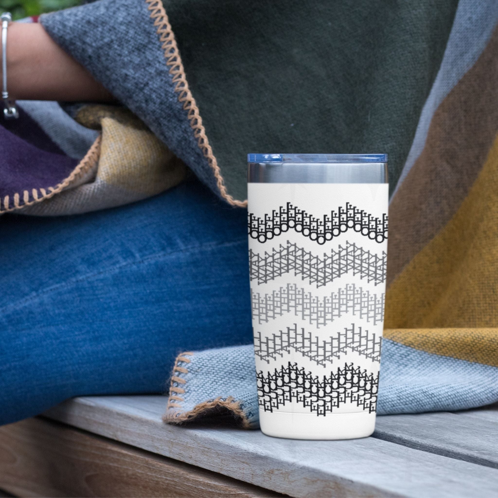 Gray stripe hidden profanity tumbler on wooden bench next to denim blanket and wool throw showing full cross stitch chevron wrap