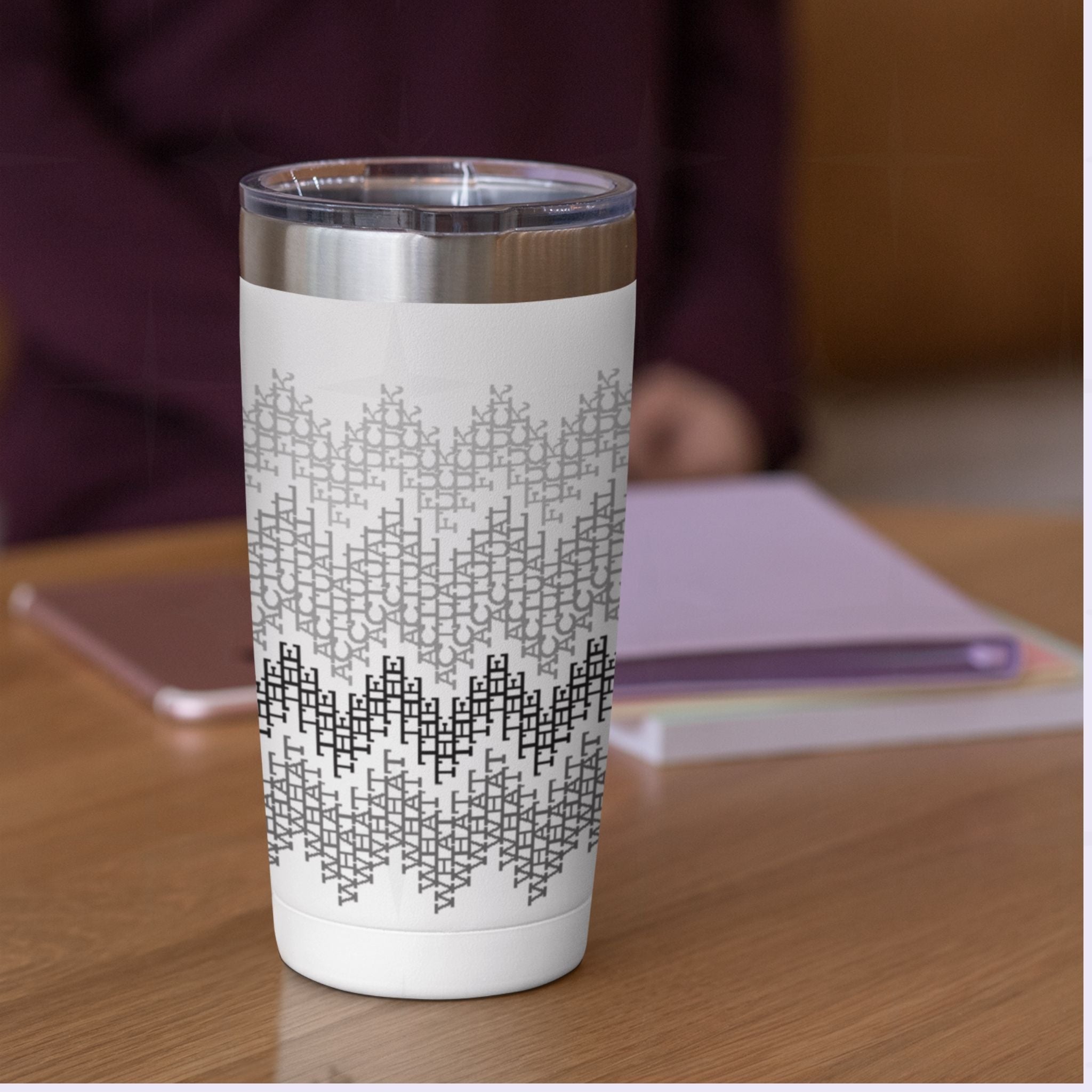 Gray stripes hidden profanity tumbler on wooden desk beside notebooks, office lifestyle setting with cross-stitch swear word pattern visible