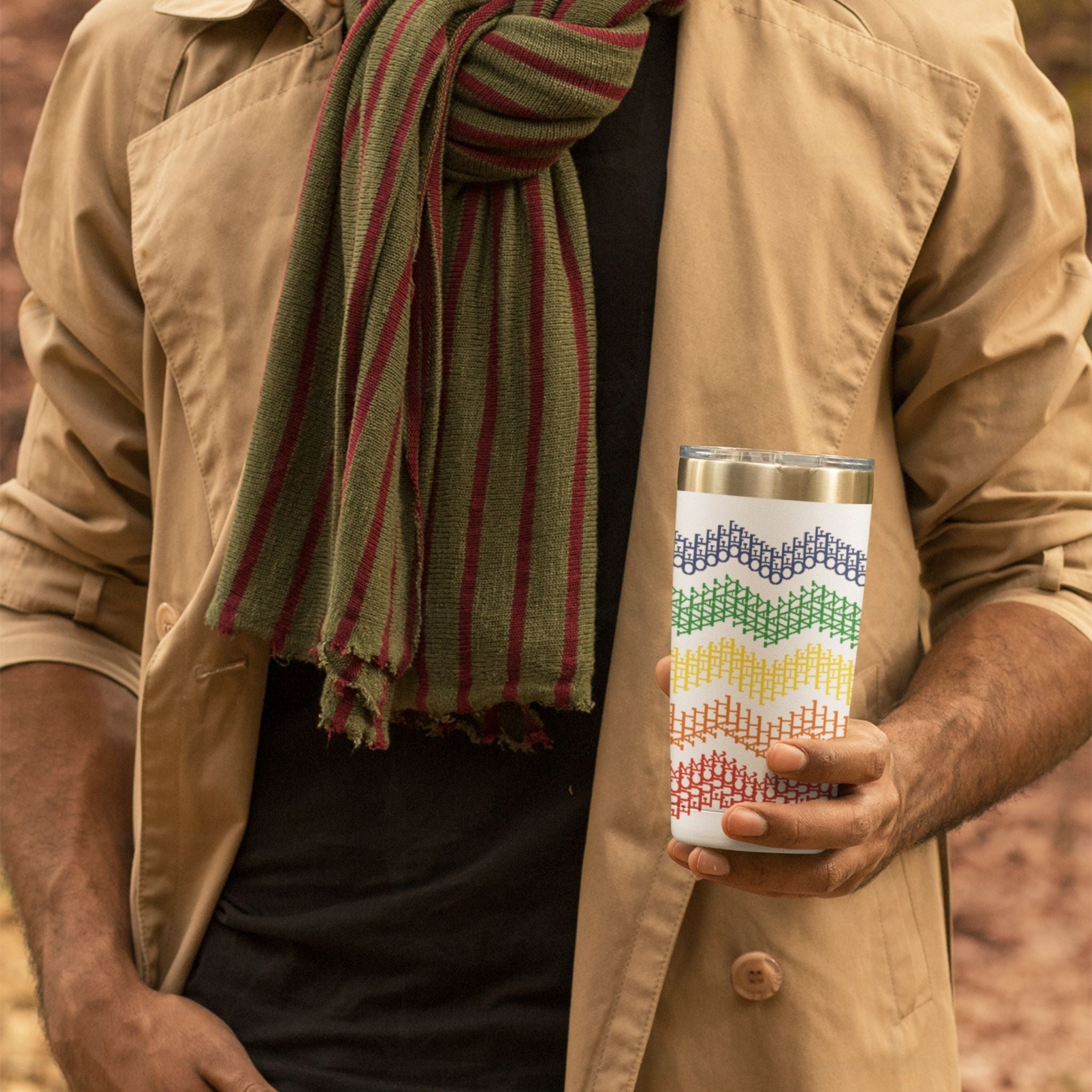 Person in tan jacket holding rainbow stripe hidden profanity tumbler outdoors showing cross stitch chevron pattern in full rainbow gradient