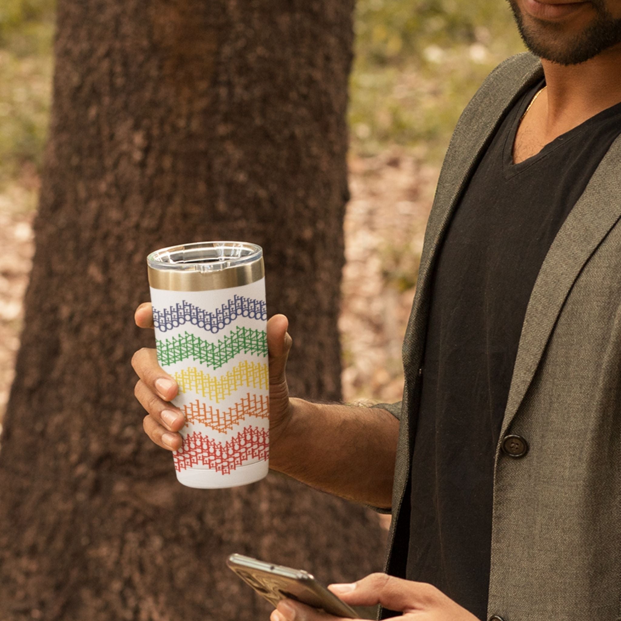 man holding rainbow stripe hidden profanity 20 oz tumbler outdoors showing blue green yellow orange red cross stitch chevron design