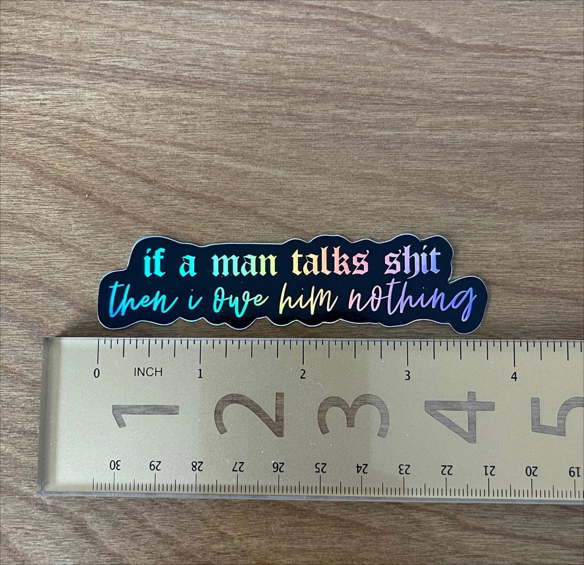 If a man talks shit then I owe him nothing holographic sticker detail — rainbow shift across the holographic vinyl under bold lettering by indie artist MangoIllustrated