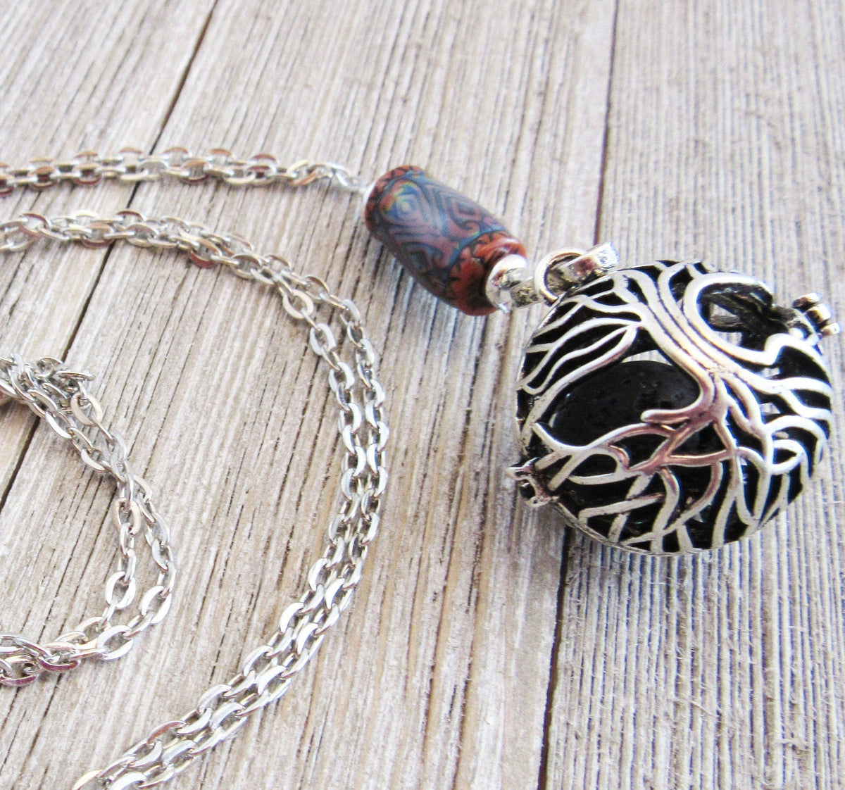 The Tree of Life Essential Oil Diffuser Necklace features a color-changing gemstone and artisan design, with an intricate tree overlay pendant, displayed on a weathered wooden surface.