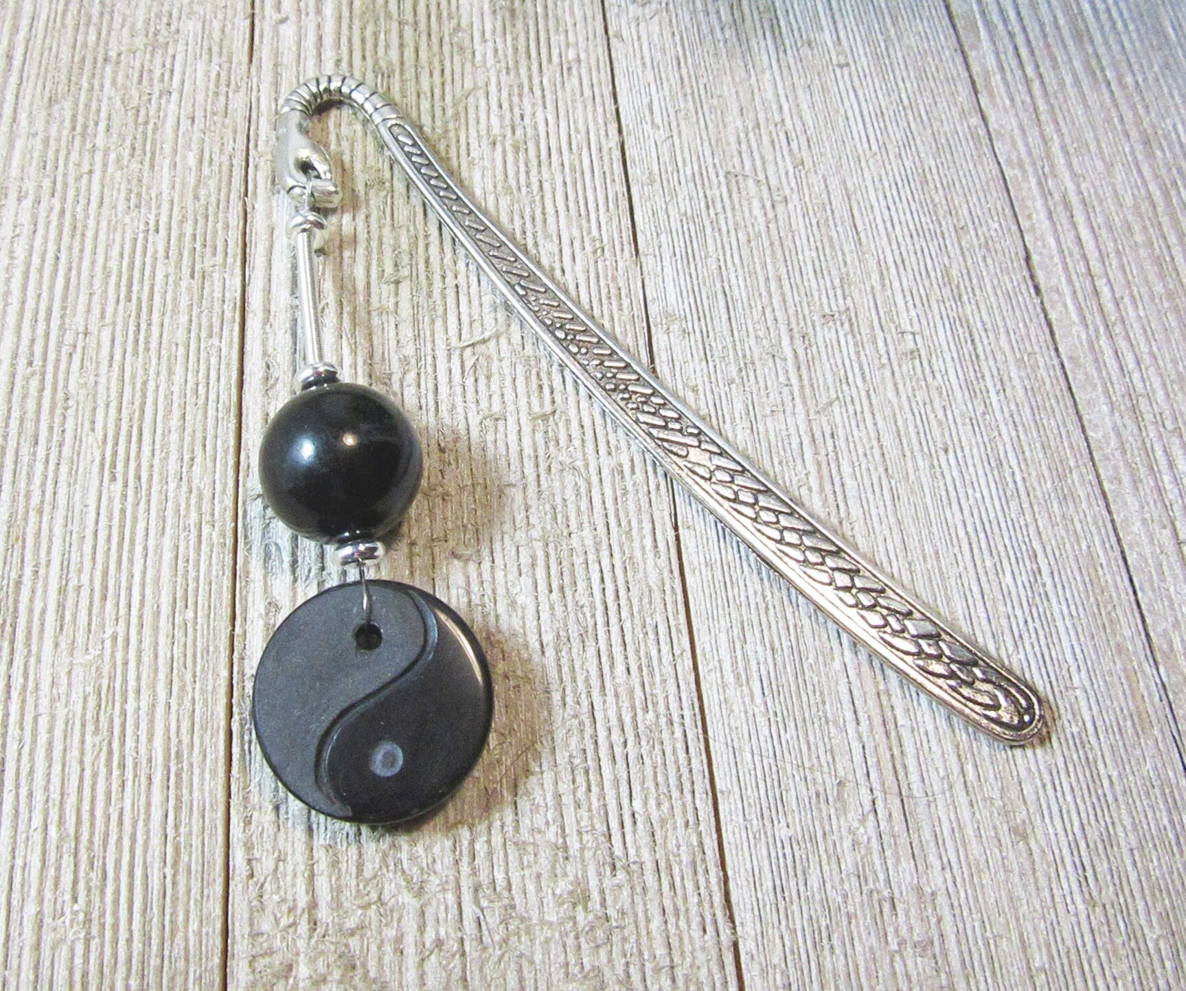The Yin Yang Bookmark: Natural Stone Accents, Zen Gift Artisan Designed, features a silver metal body with textured handle, black round natural stone bead, and yin-yang charm, displayed on a light wood surface.