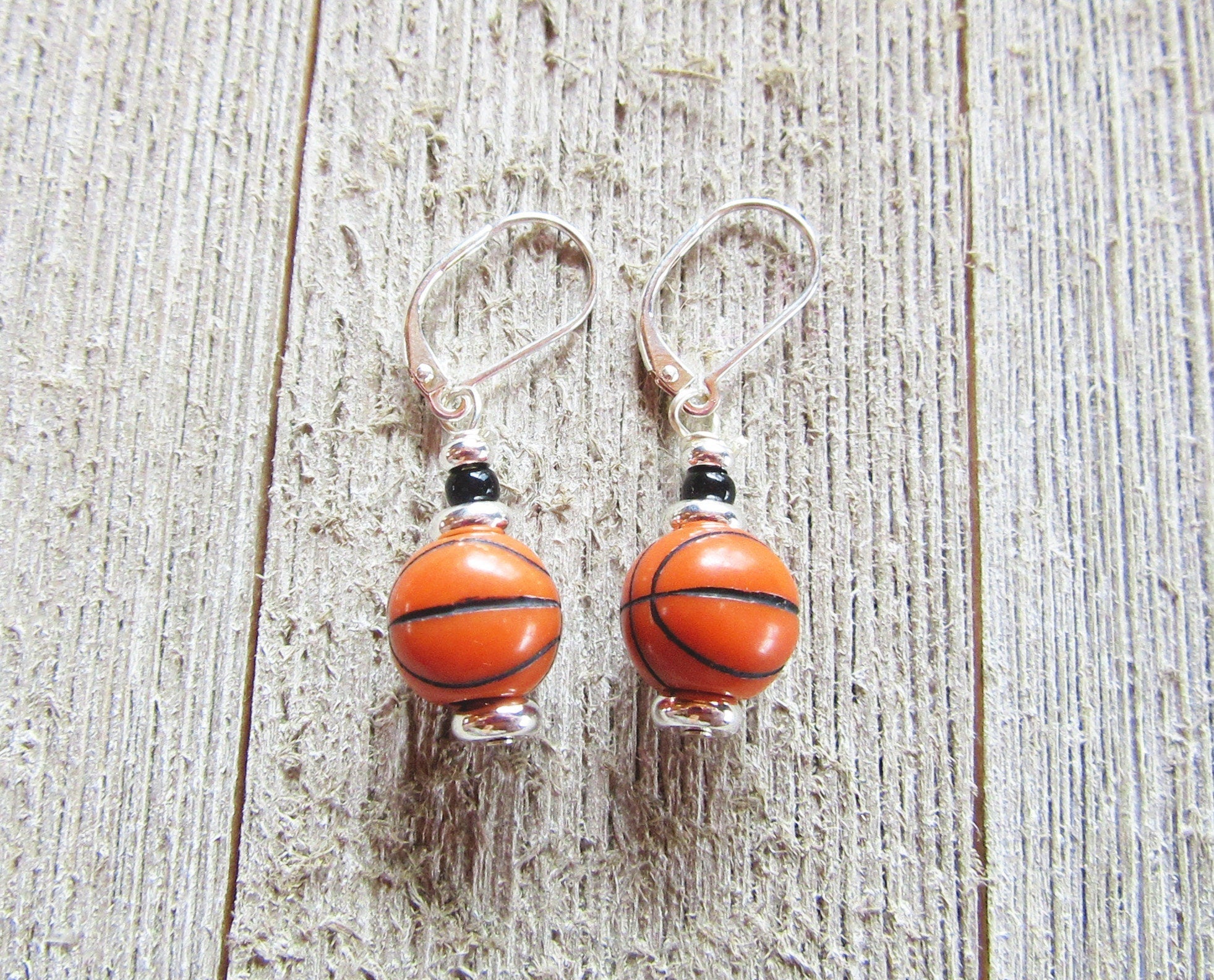 Hand-crafted Basketball Earrings—sports jewelry with small basketball-shaped beads and sterling silver lever backs—displayed on a rustic wooden surface.
