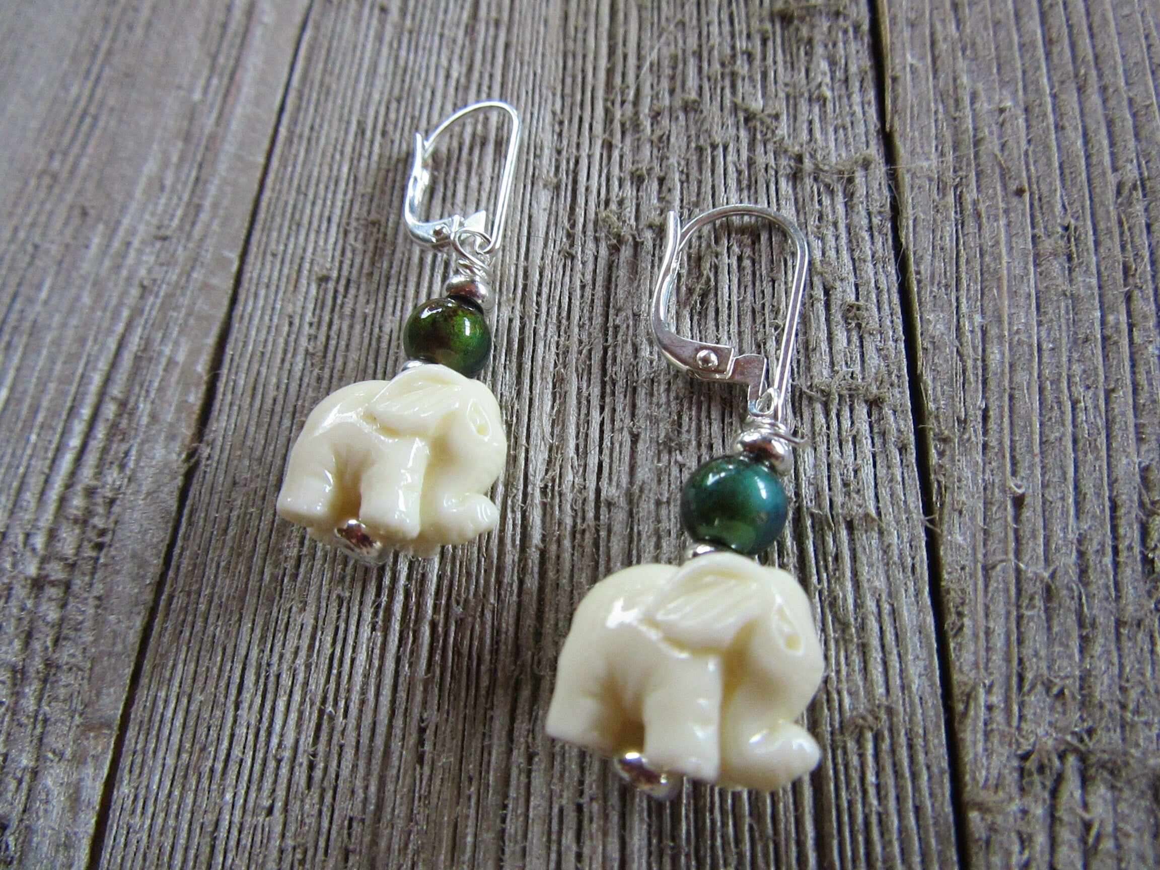 Elephant Earrings – Boho Mood Beads feature cream elephant charms and a sterling silver color change topper bead, displayed on rustic wood. Only one pair available.