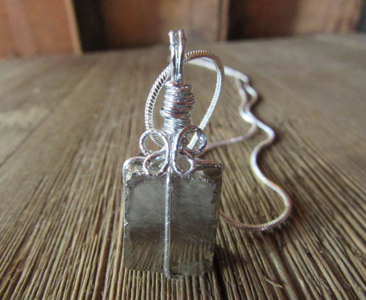 The Chunky Pyrite Crystal Pendant, a handcrafted zen necklace with a 16-18 inch chain, showcases a bold pyrite stone wrapped in silver wire and displayed on wood, its natural beauty accentuated by the softly blurred background.