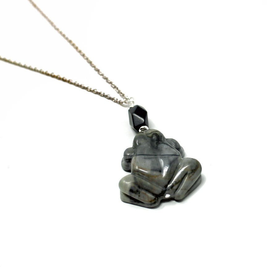 The Jasper Frog Pendant: Handmade Animal Lover Necklace features a silver chain with a carved natural jasper stone frog and a small black faceted bead, shown on a white background.