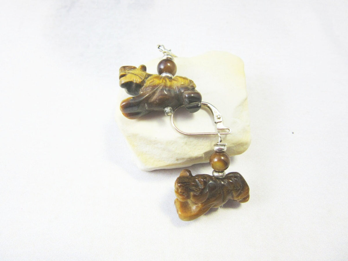 Tiger Eye Stone Earrings: Sterling Silver Lever Back—carved brown animal figures and round beads, perfect for animal lovers. Displayed on a smooth pale stone against a white background.