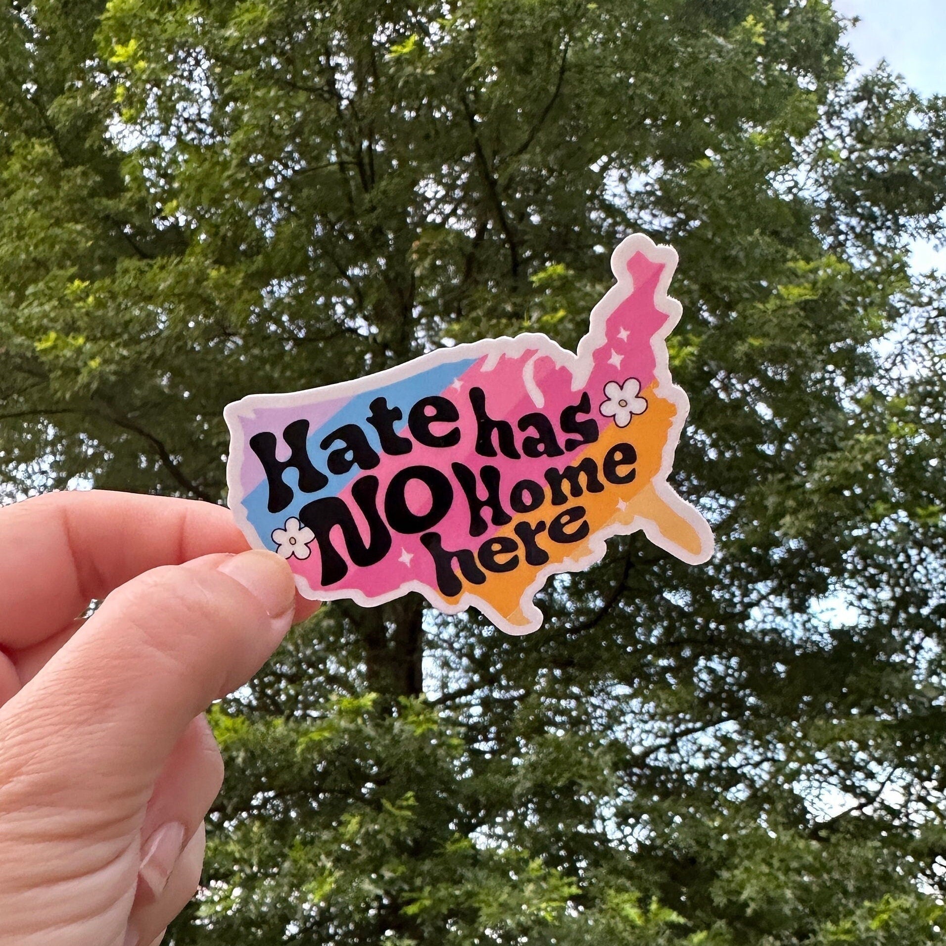 Hate Has No Home Here text in a colorful drawing of the shape of the continental United States, being held by a hand.