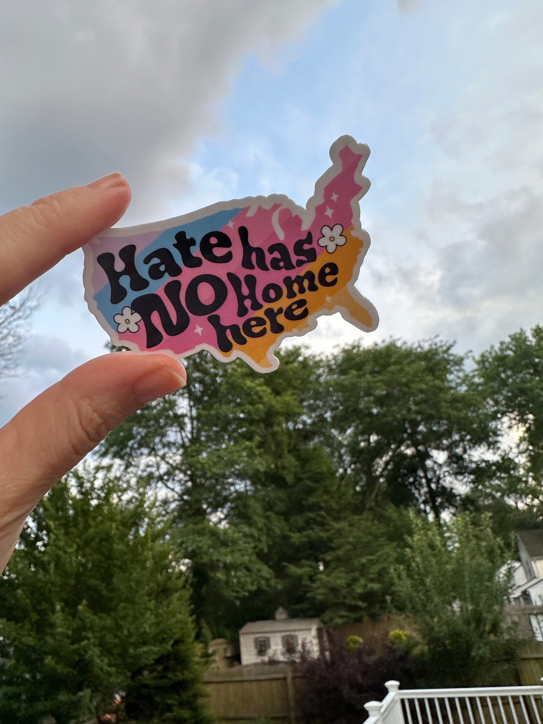 Hate Has No Home Here text in a colorful drawing of the shape of the continental United States, being held by a hand.