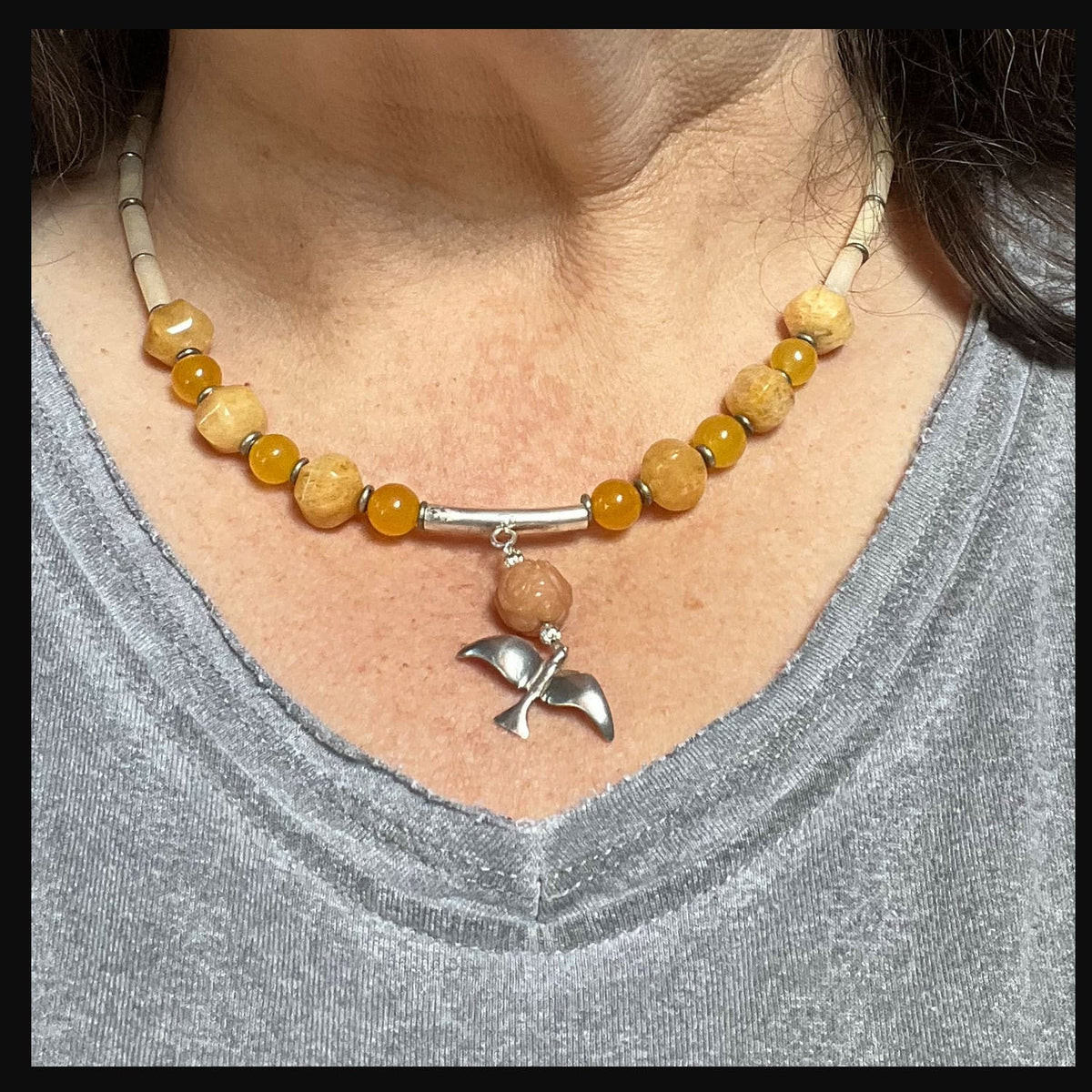 Close-up view of the Silver Bird in Flight Necklace showcasing vibrant orange and yellow stones and sterling silver bird charm.
