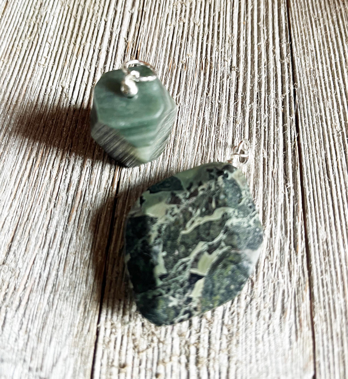 The Chunky Style Masc Forest Green Stone Pendant—an earthy gemstone on a 5mm cord with a silver bail—rests on rustic, light wood, showcasing its forest green color and marbled finish for an eye-catching natural necklace.