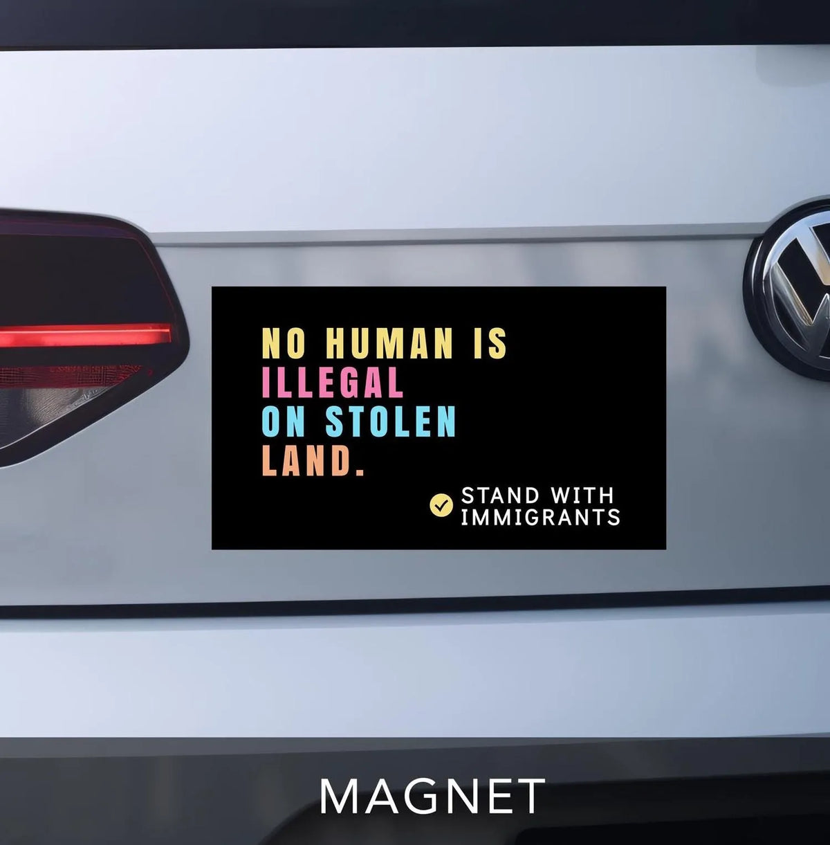 No human is illegal on stolen land magnet for car bumper. black with pastel block lettering. reads "stand with immigrants" in bottom right corner.