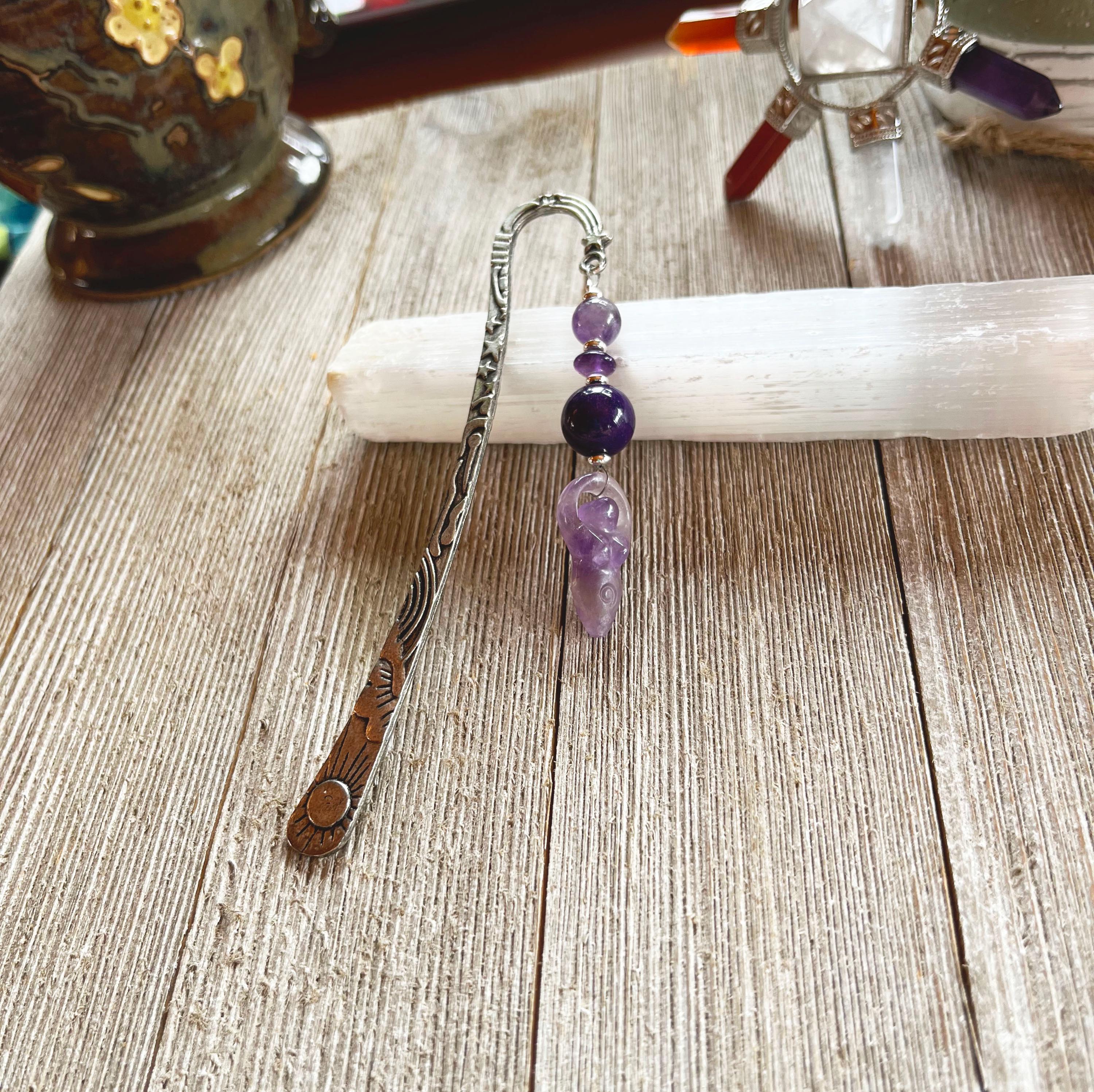 The Amethyst Bookmark: Artisan Designed Divine Goddess Celestial Gift features engraved metal, purple beads, and an amethyst angel charm, pictured on a white selenite stick—making it a perfect celestial-themed present.