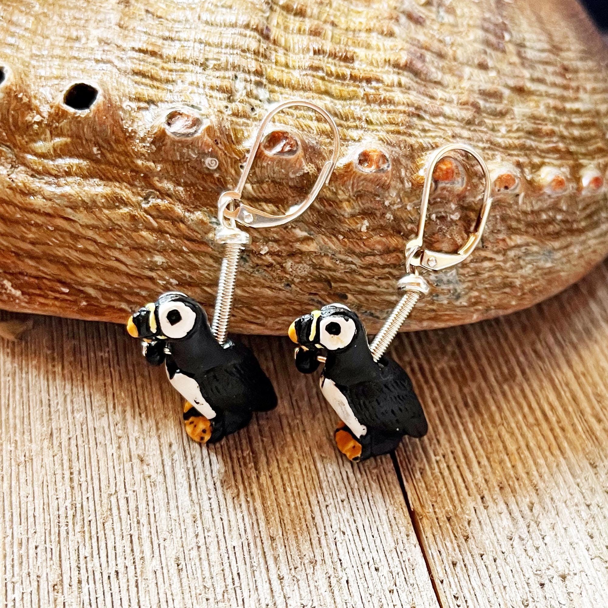 Handpainted Puffin Earrings—charming puffin bird charms on silver hooks—are displayed with a seashell and wood backdrop, making a perfect marine bird lover gift.