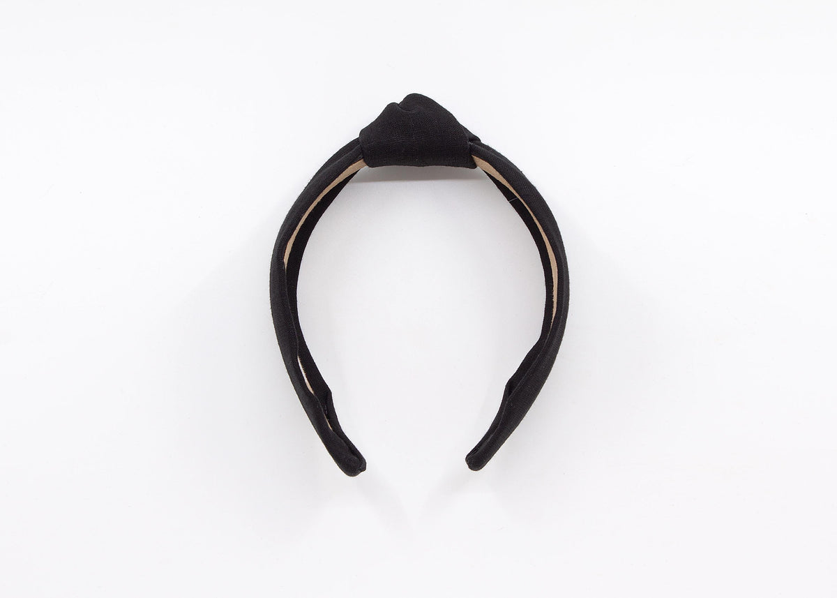 May include: A black knotted headband made of linen fabric. The headband has a label that says "MADDIE AND ME".