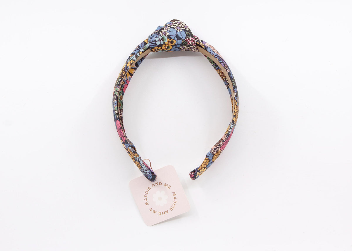 A floral print headband with a knotted design. The headband has a tag that says "MADDIE AND ME".