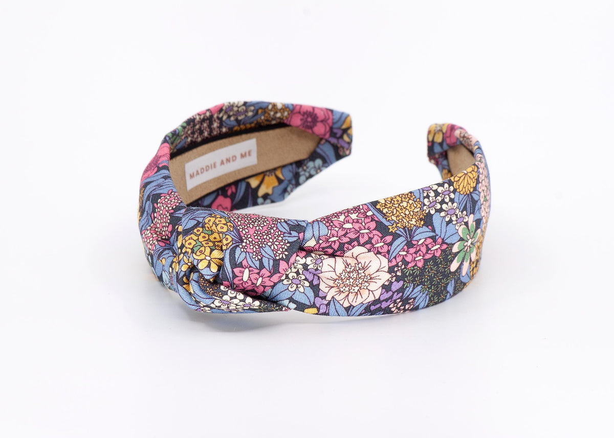 A floral print headband with a knotted design. The headband has a label that says "MADDIE AND ME".