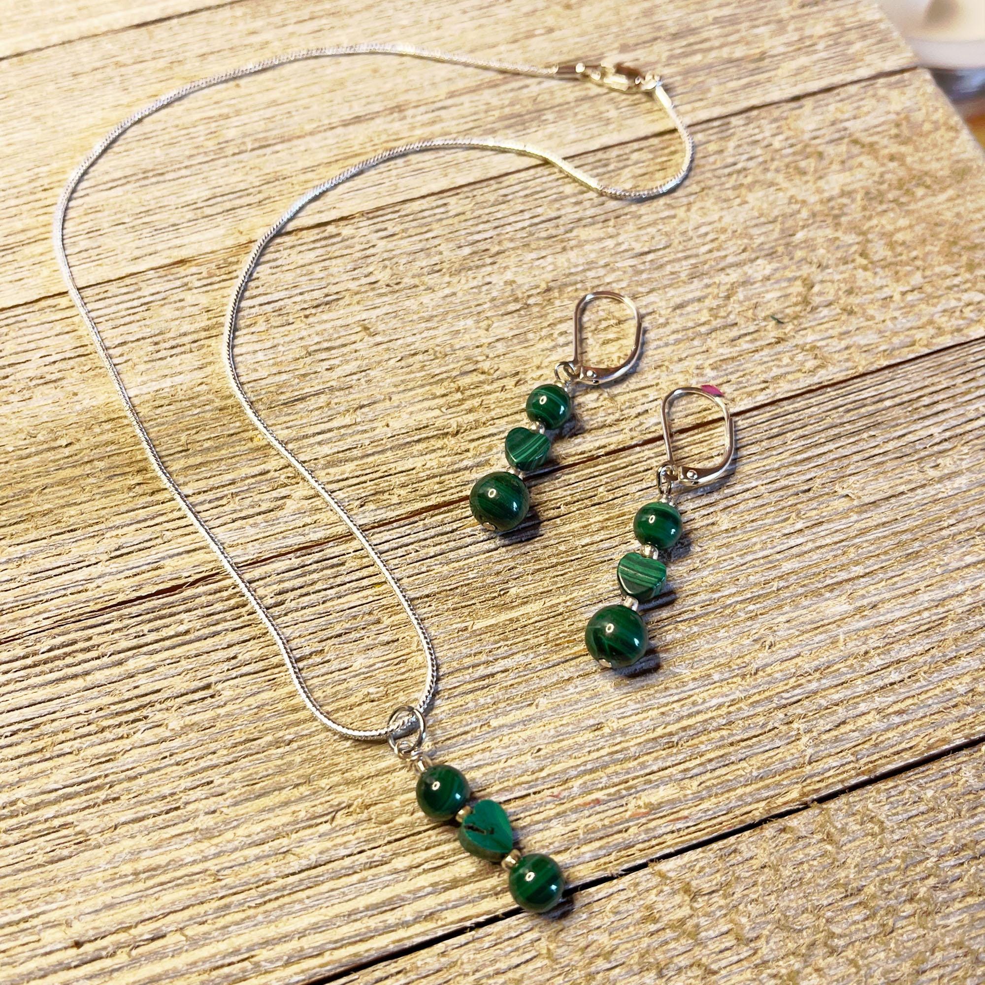The Green Malachite Heart Jewelry Set features a Spring Dangle Necklace with three green striped beads in a row and matching earrings with two beads each—an elegant handcrafted set displayed on light wood, perfect for any occasion.