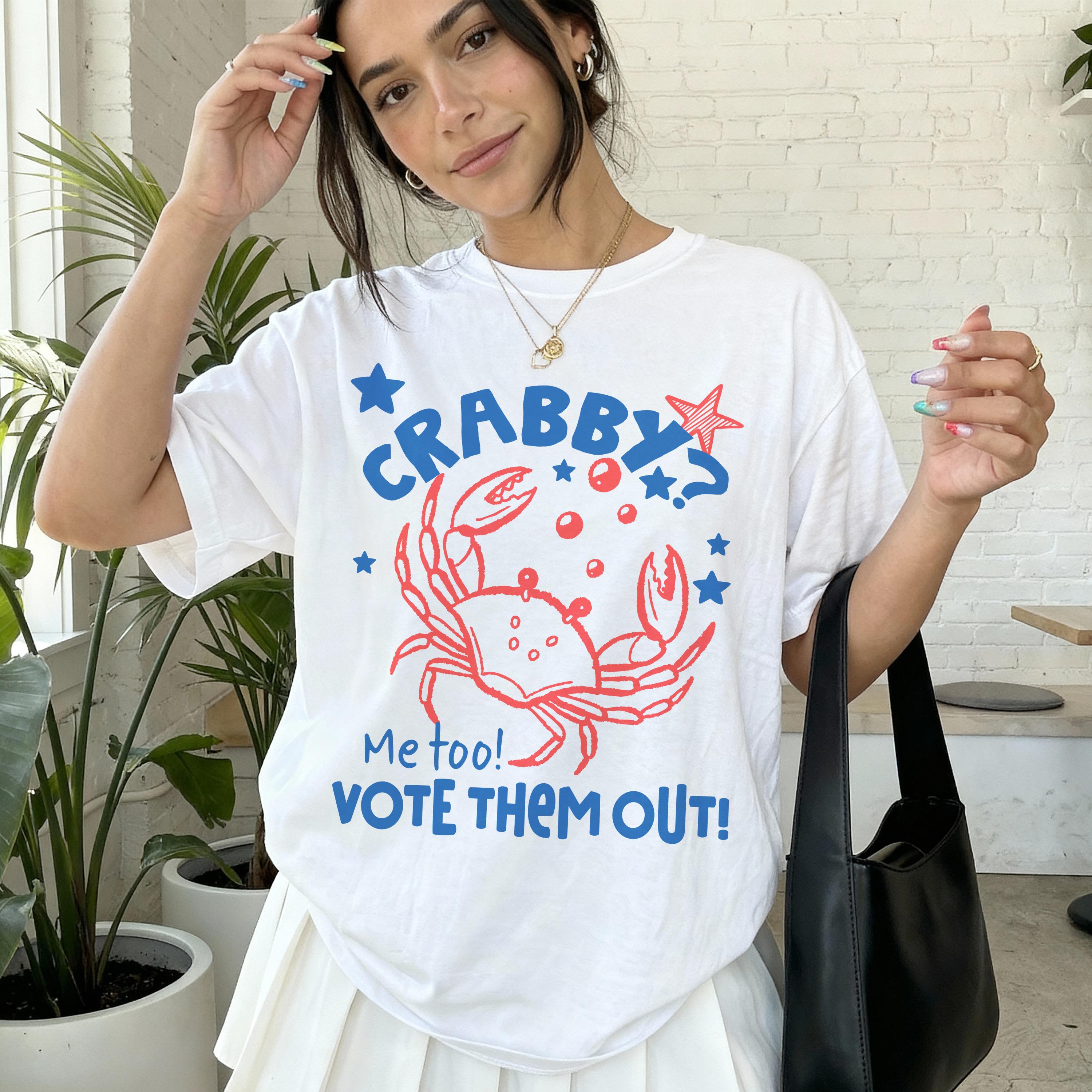 Woman wearing white t-shirt with red crab graphic and "Me too! Vote Them Out!" text.