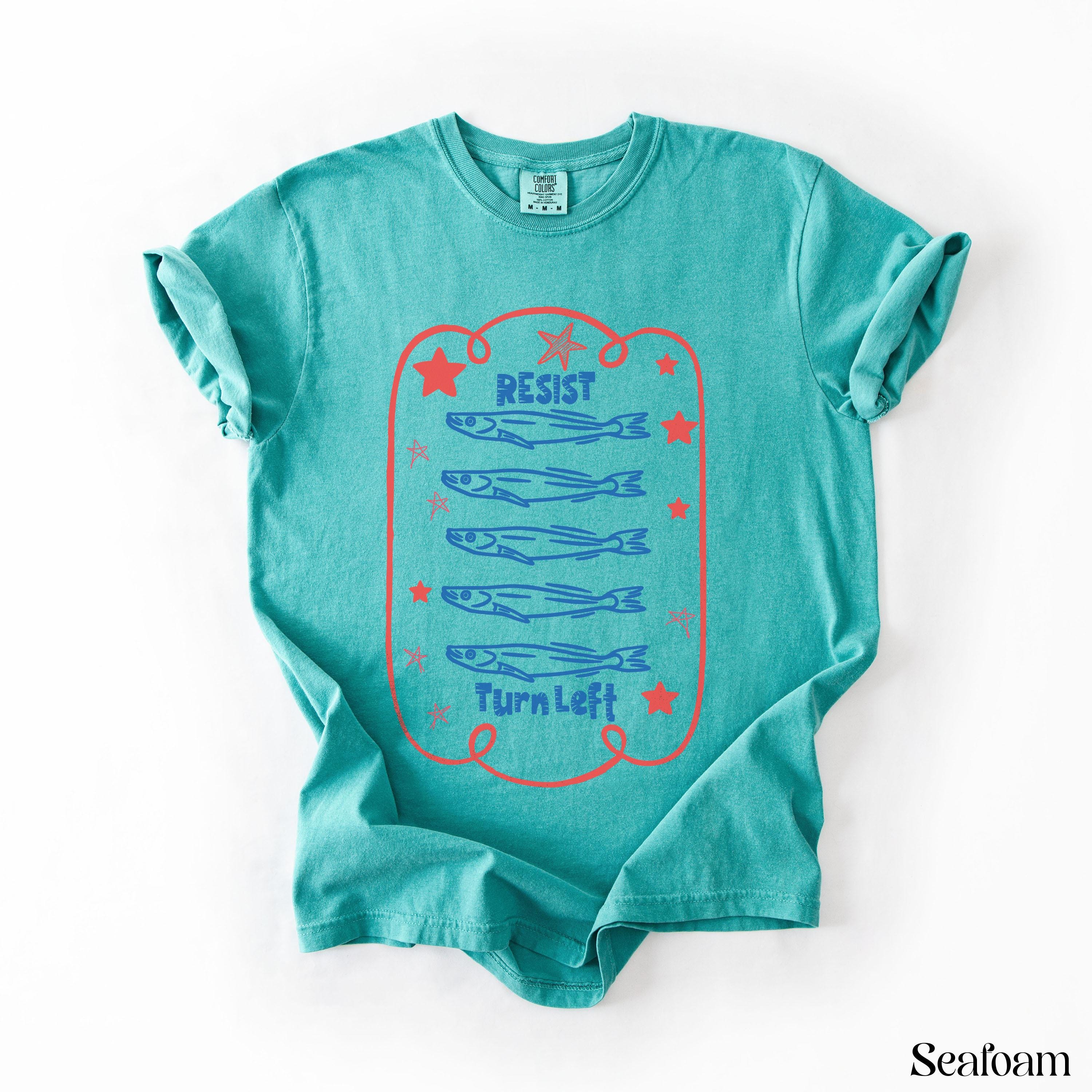 Teal t-shirt with red border, stars, and three rows of blue fish and "Resist Turn Left" text.