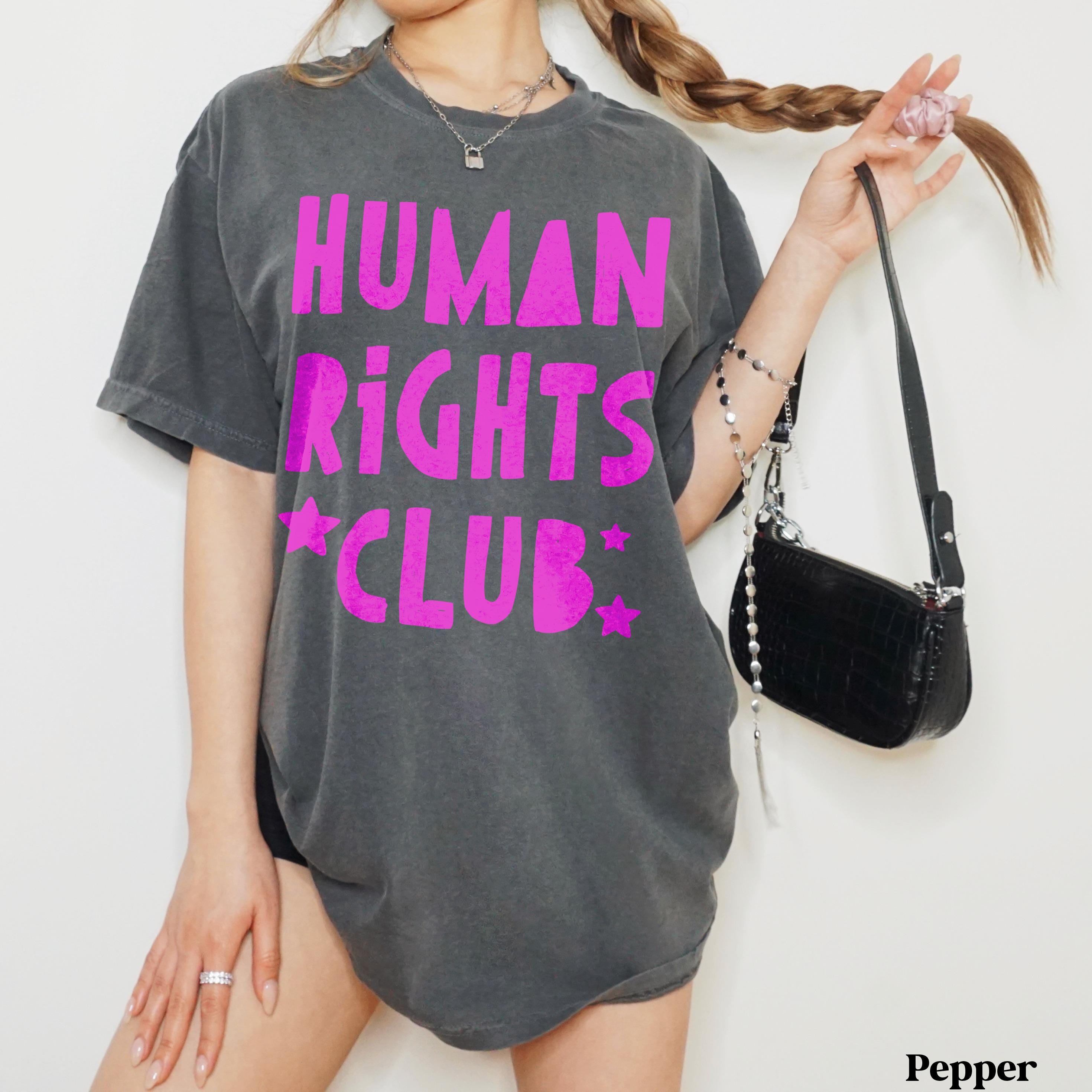 Woman in dark grey t-shirt with bright pink "Human Rights Club" text and stars.