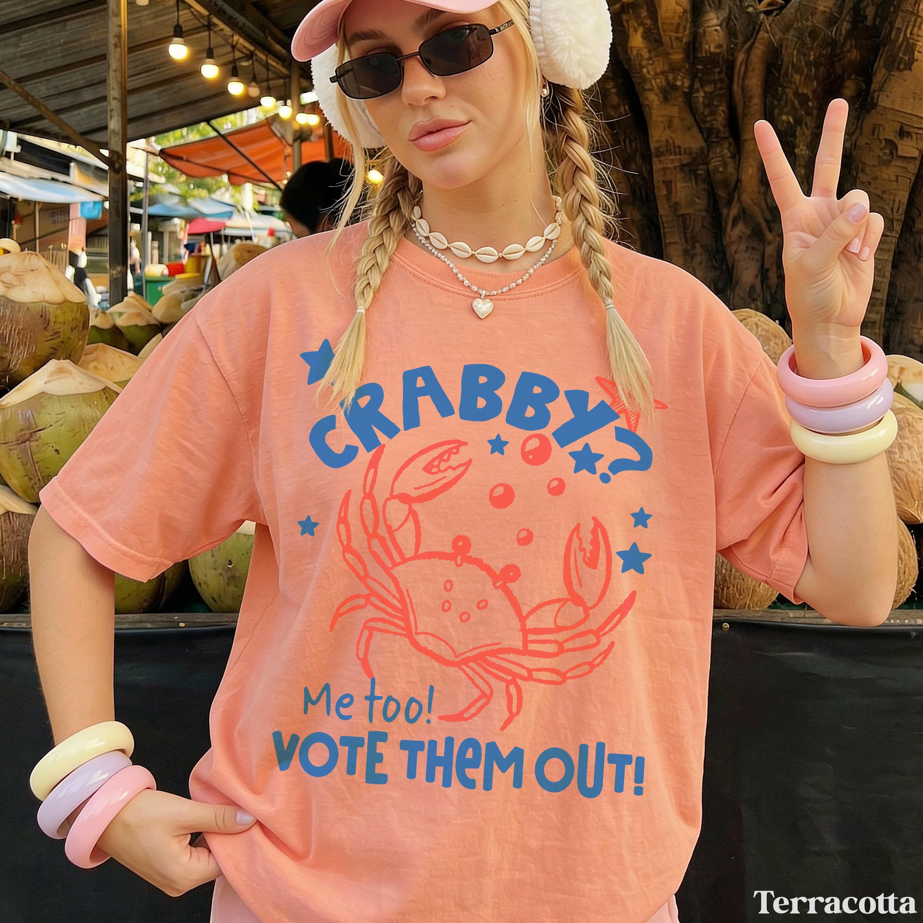 Woman in coral t-shirt saying "Crabby? Me too! Vote Them Out!" with peace sign.