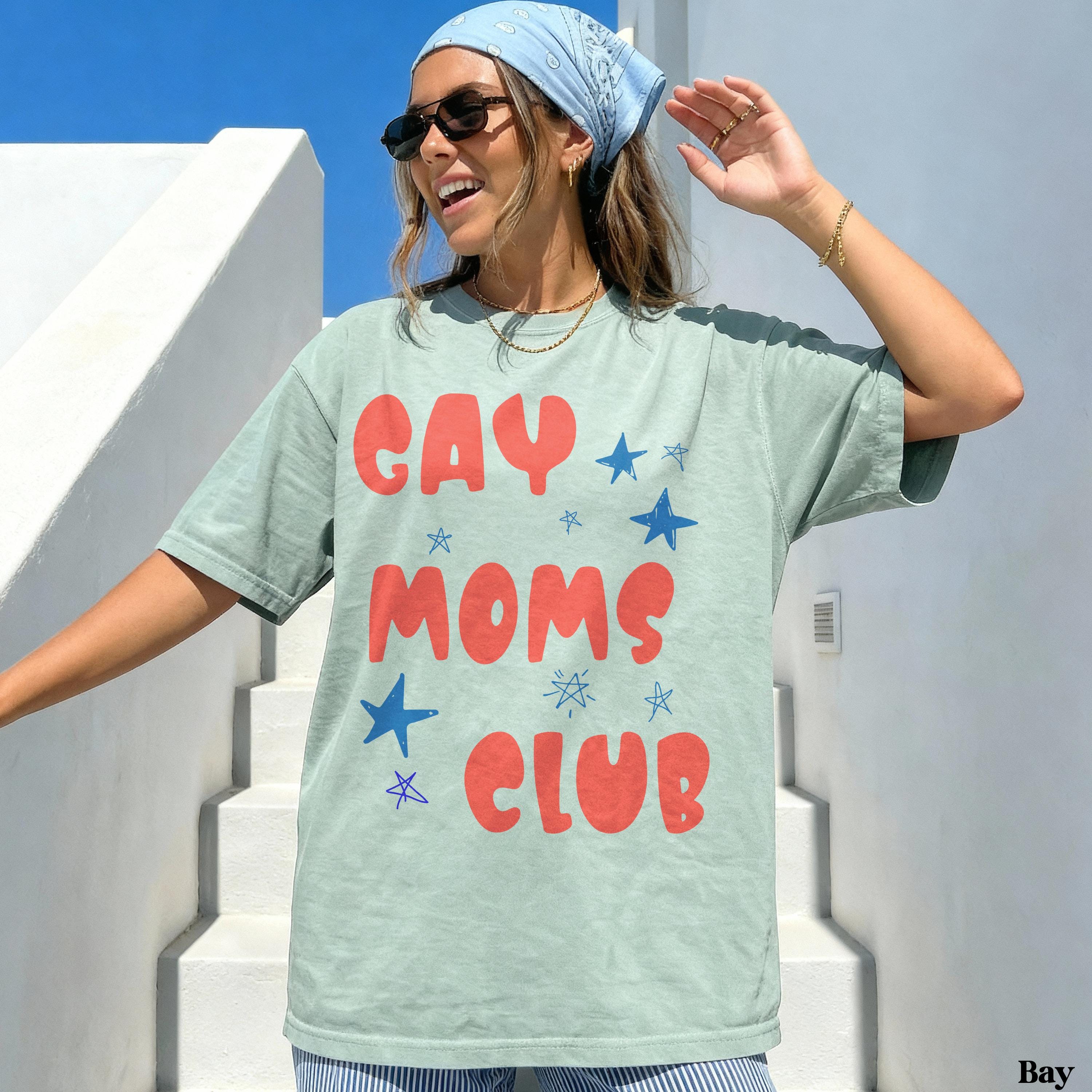 Woman wearing a light green t-shirt with "Gay Moms Club" text and blue stars.