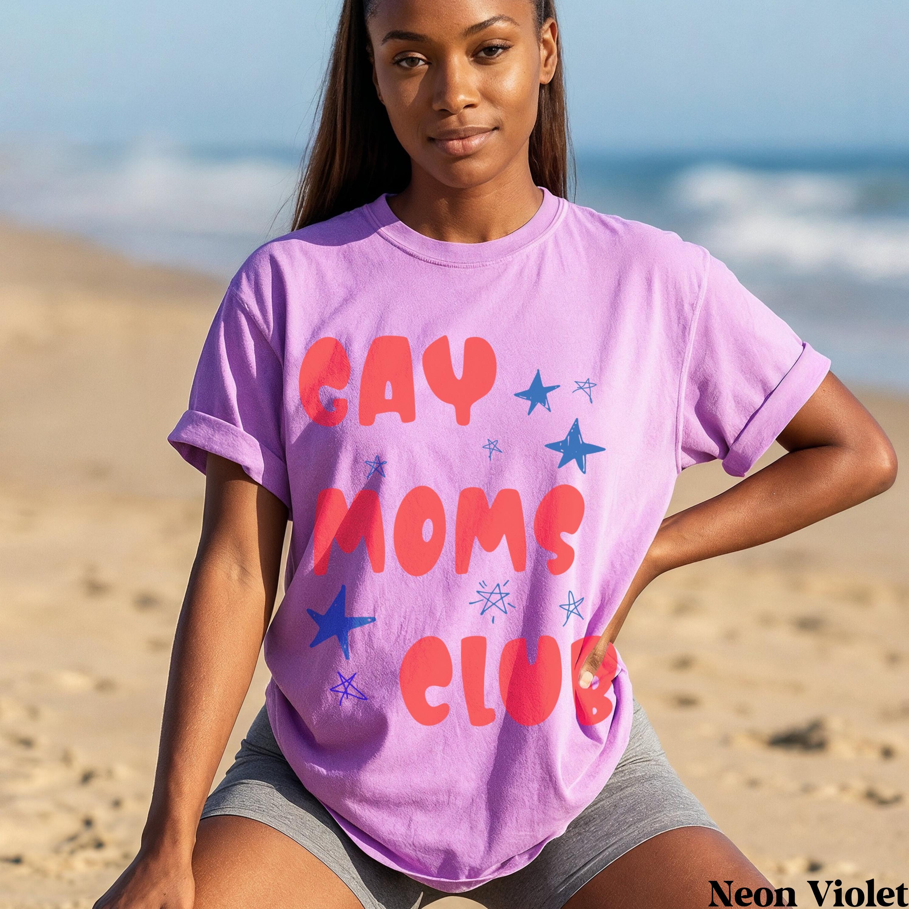 Woman wearing a purple t-shirt with "GAY MOMS CLUB" in red letters and blue stars.