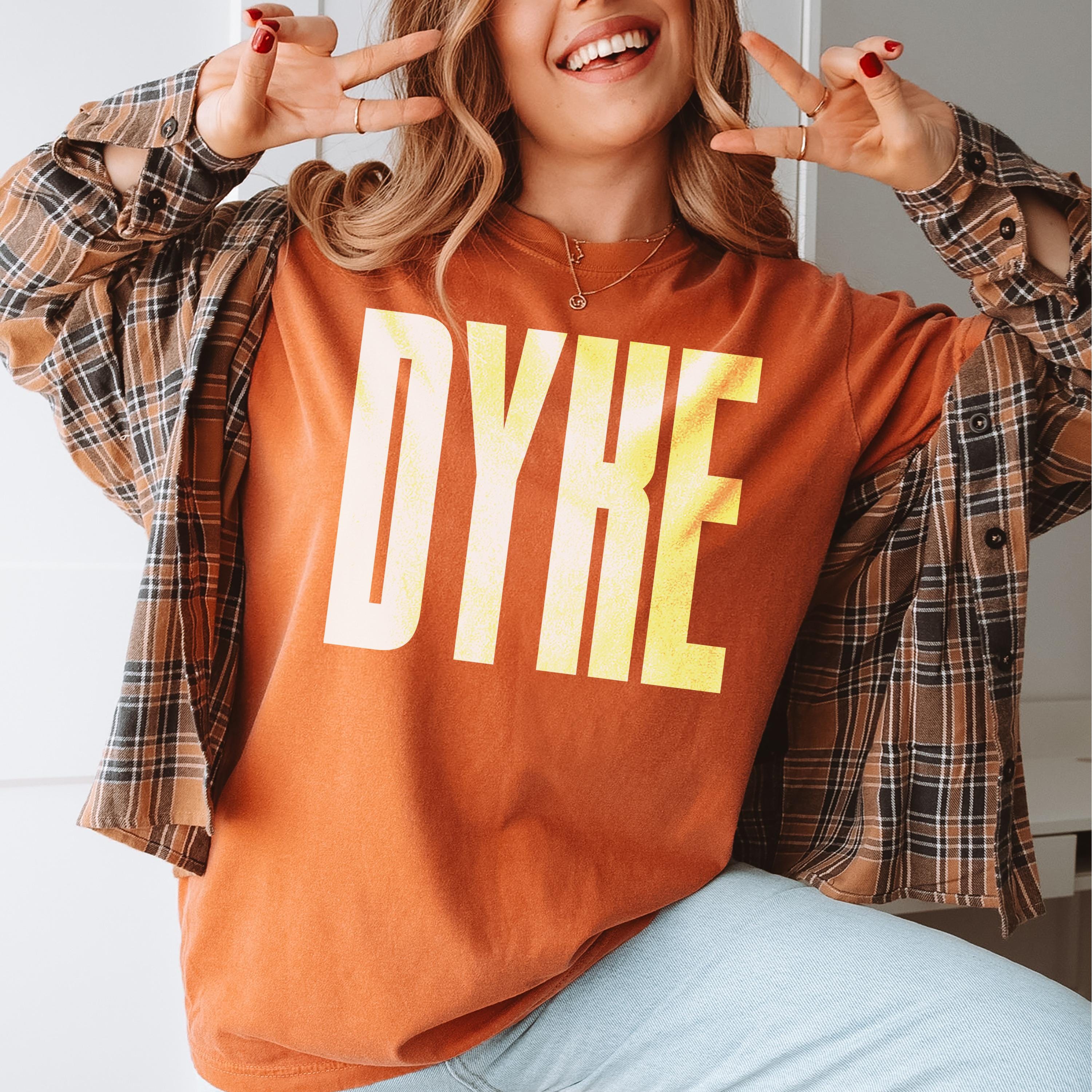 Woman wearing an orange t-shirt with "DYKE" in yellow letters.