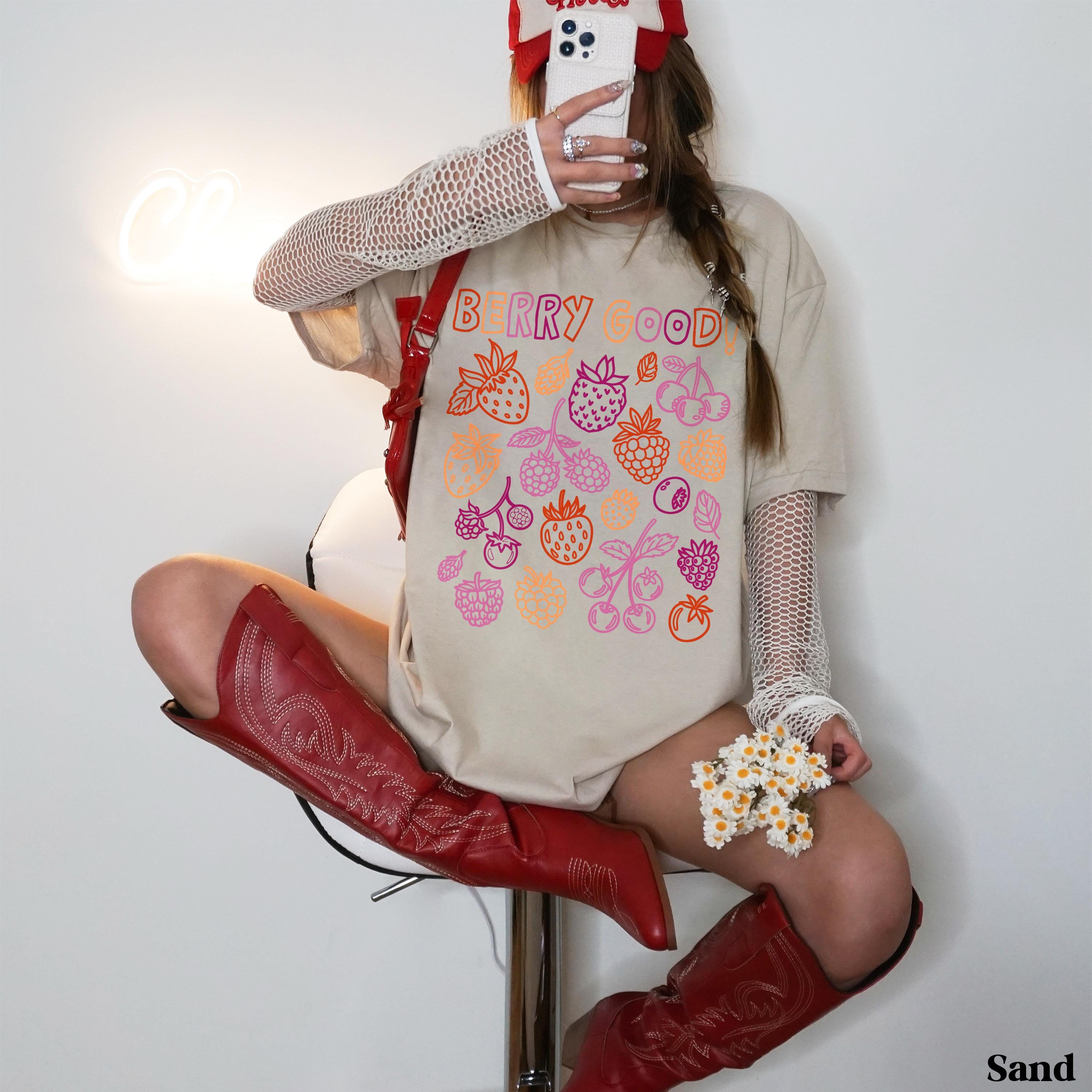 Woman in beige t-shirt with "Berry Good" text and berry illustrations, wearing red boots.