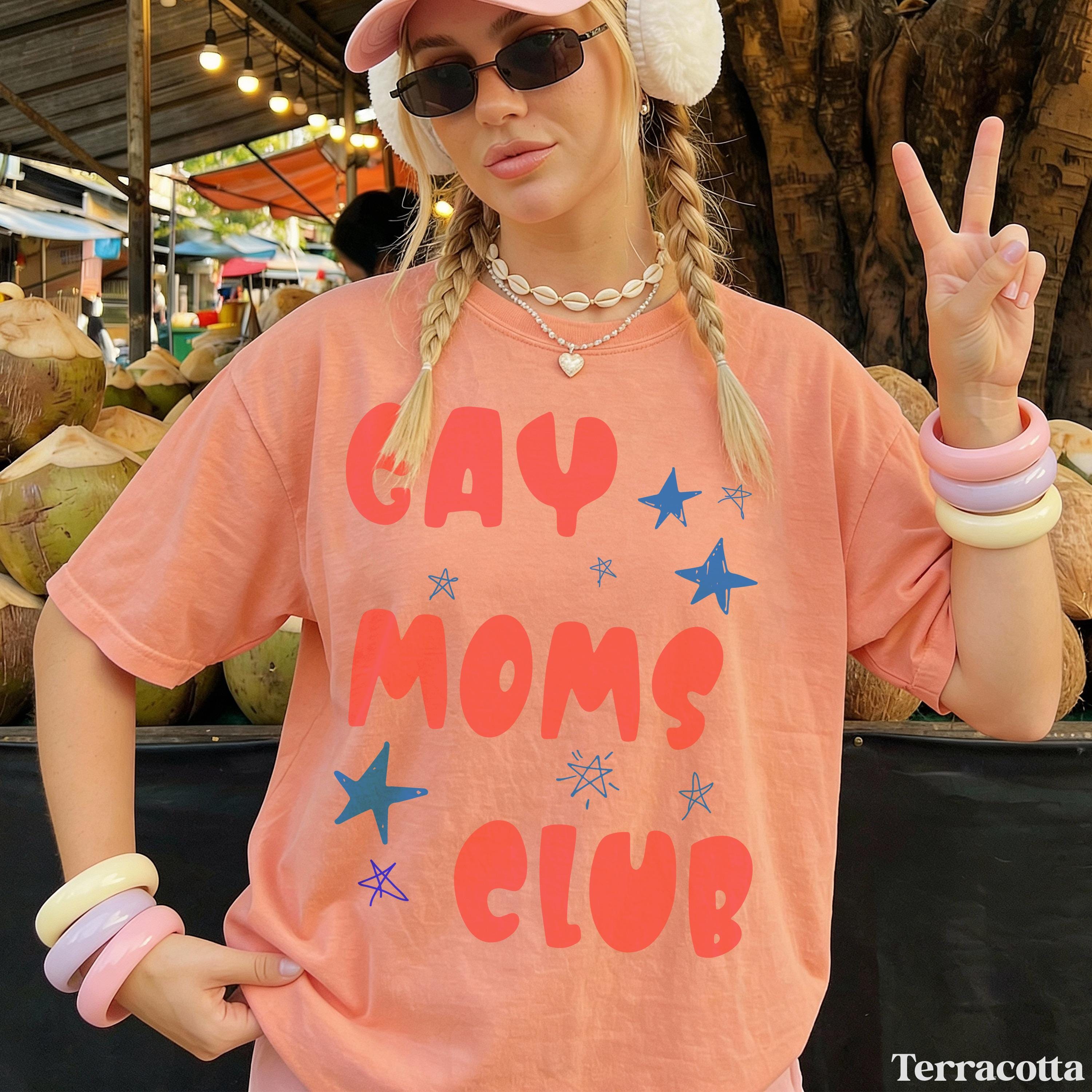 Woman wearing an orange t-shirt with "GAY MOMS CLUB" text and blue stars.