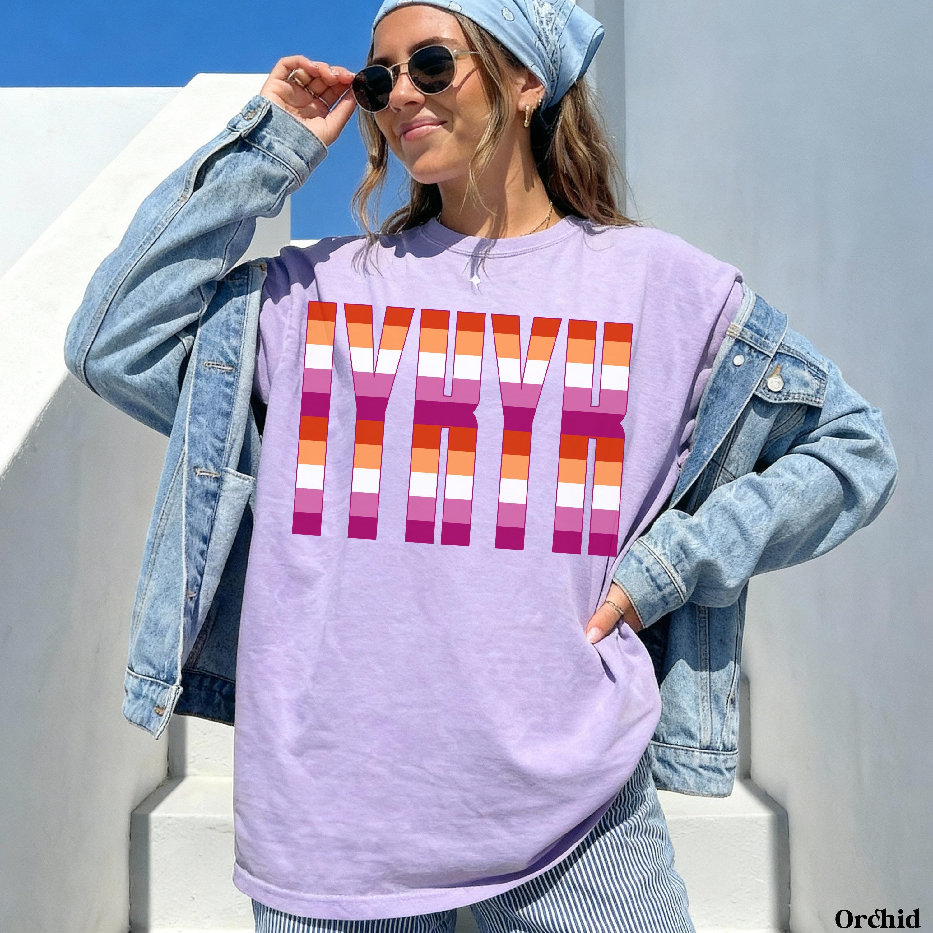 Lavender t-shirt with colorful stripes spelling "LYVV" worn by a woman.