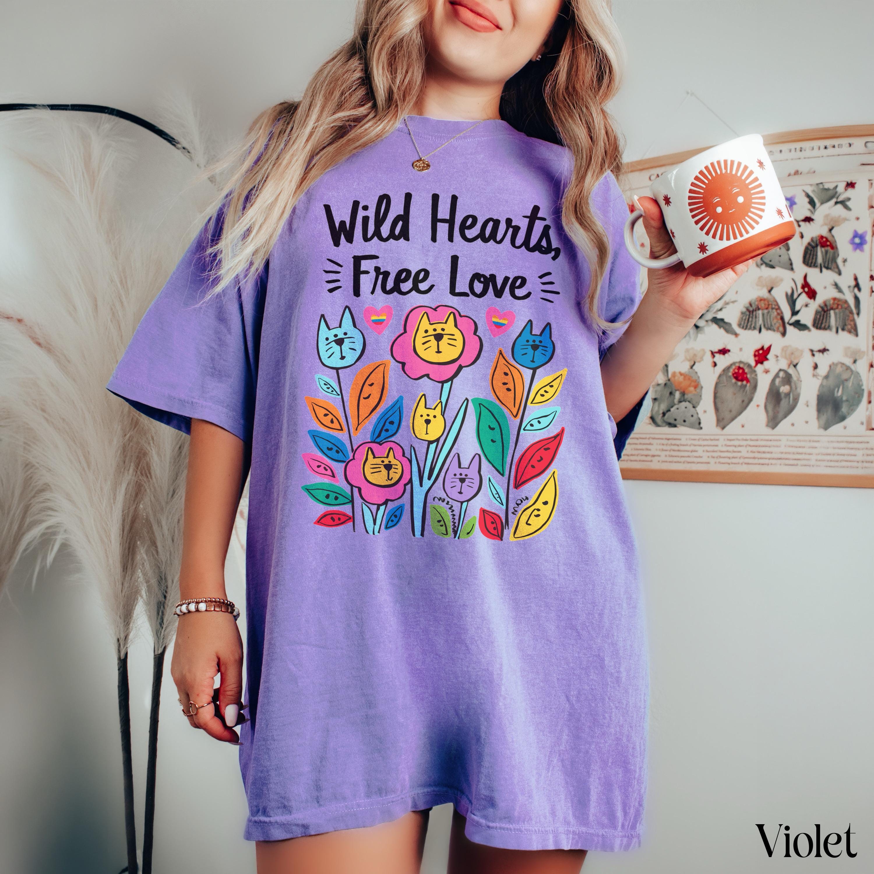 Purple t-shirt with colorful flowers and cats graphic and text "Wild Hearts, Free Love".