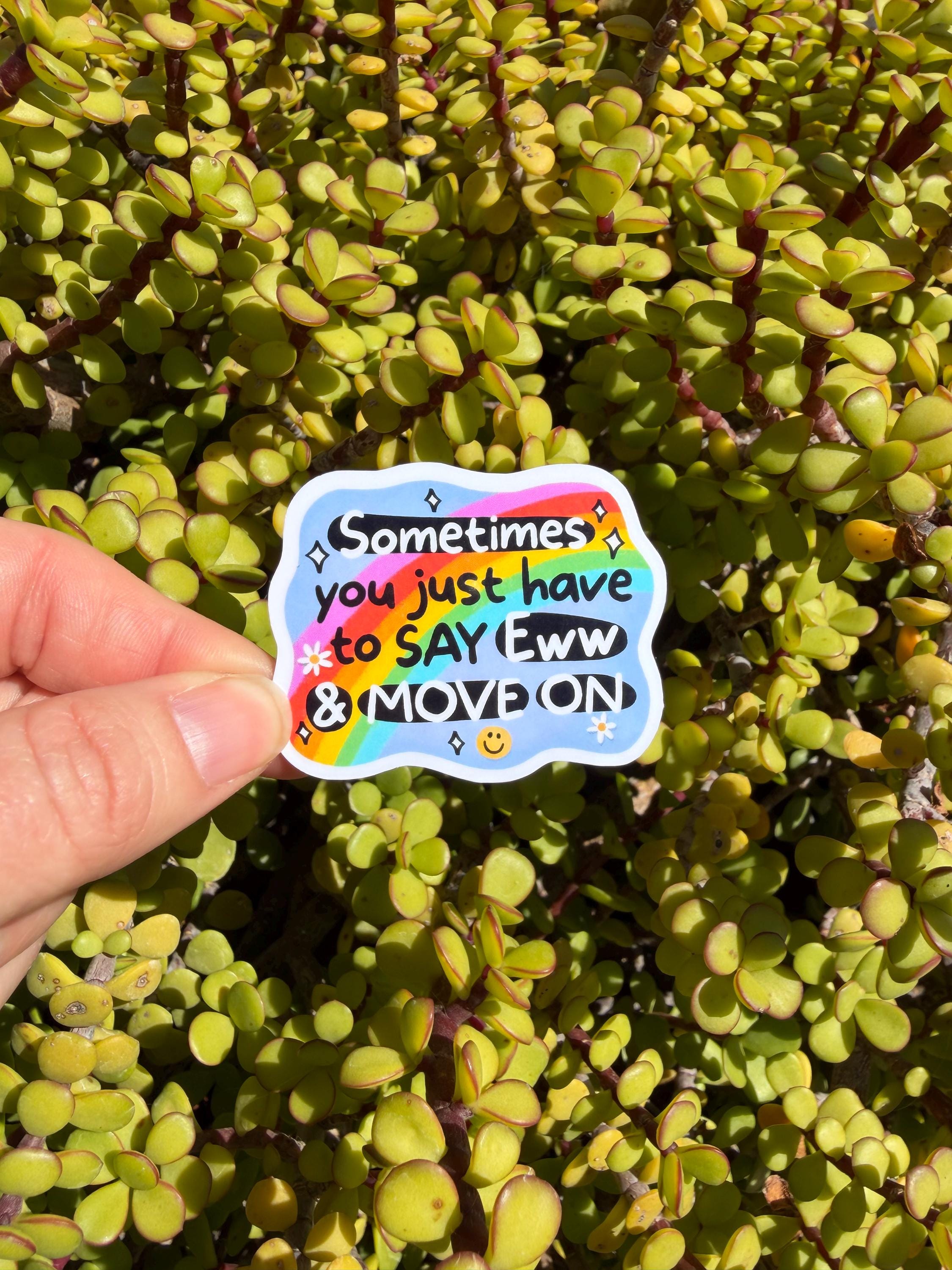 May include: A colorful sticker with the text "Sometimes you just have to say Eww & MOVE ON" over a rainbow design. The sticker is held against a background of green succulent plants.