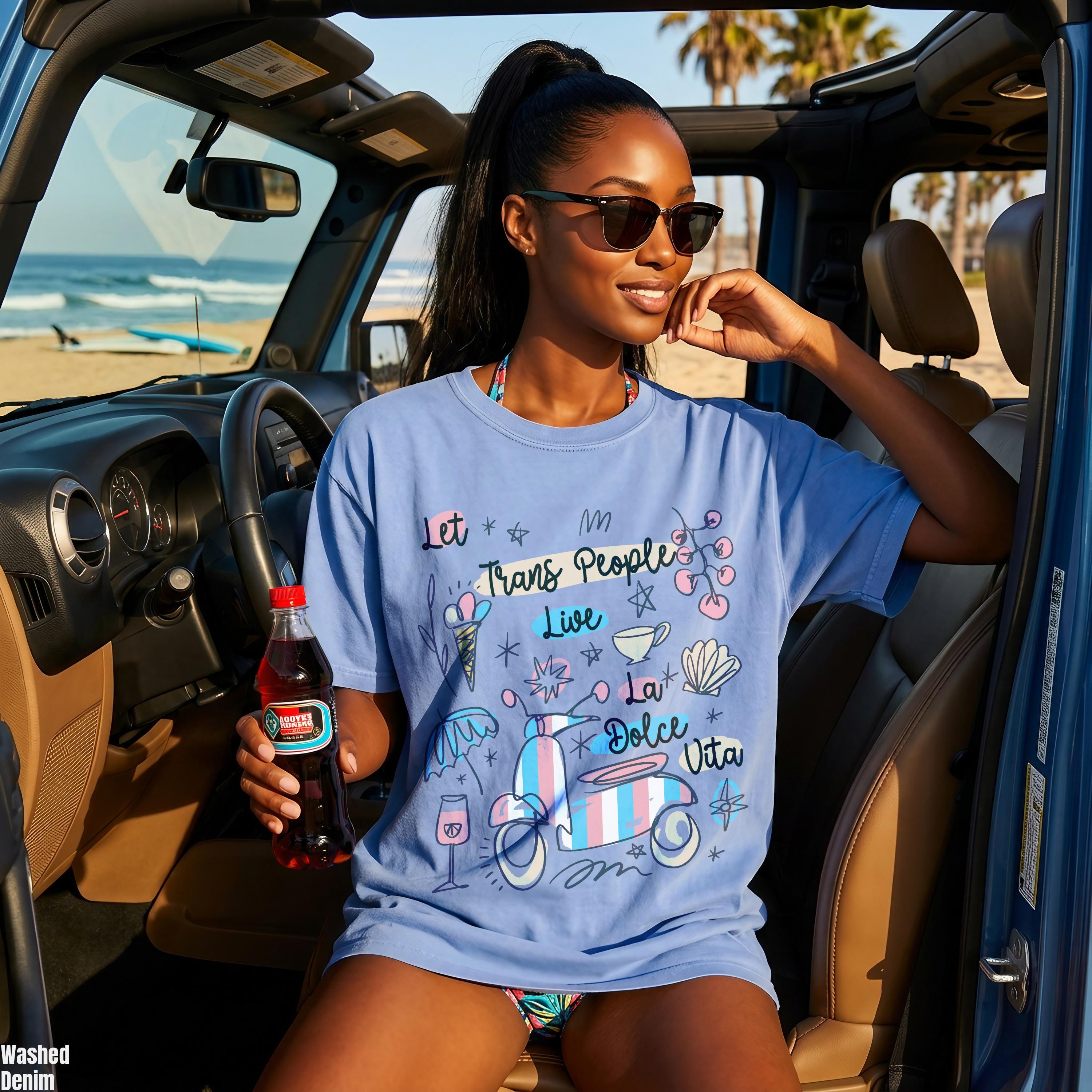 Woman in blue jeep wearing t-shirt with "Let Trans People Live" and scooter design.