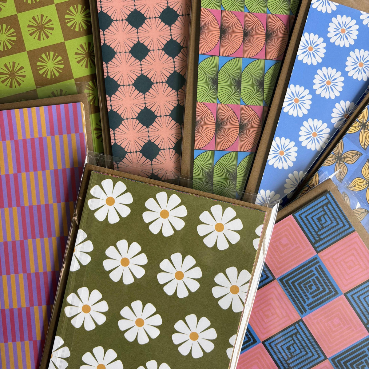 Collection of colorful retro-patterned cardstock sheets and card packs featuring floral, geometric, and checkerboard designs arranged in an overlapping display.