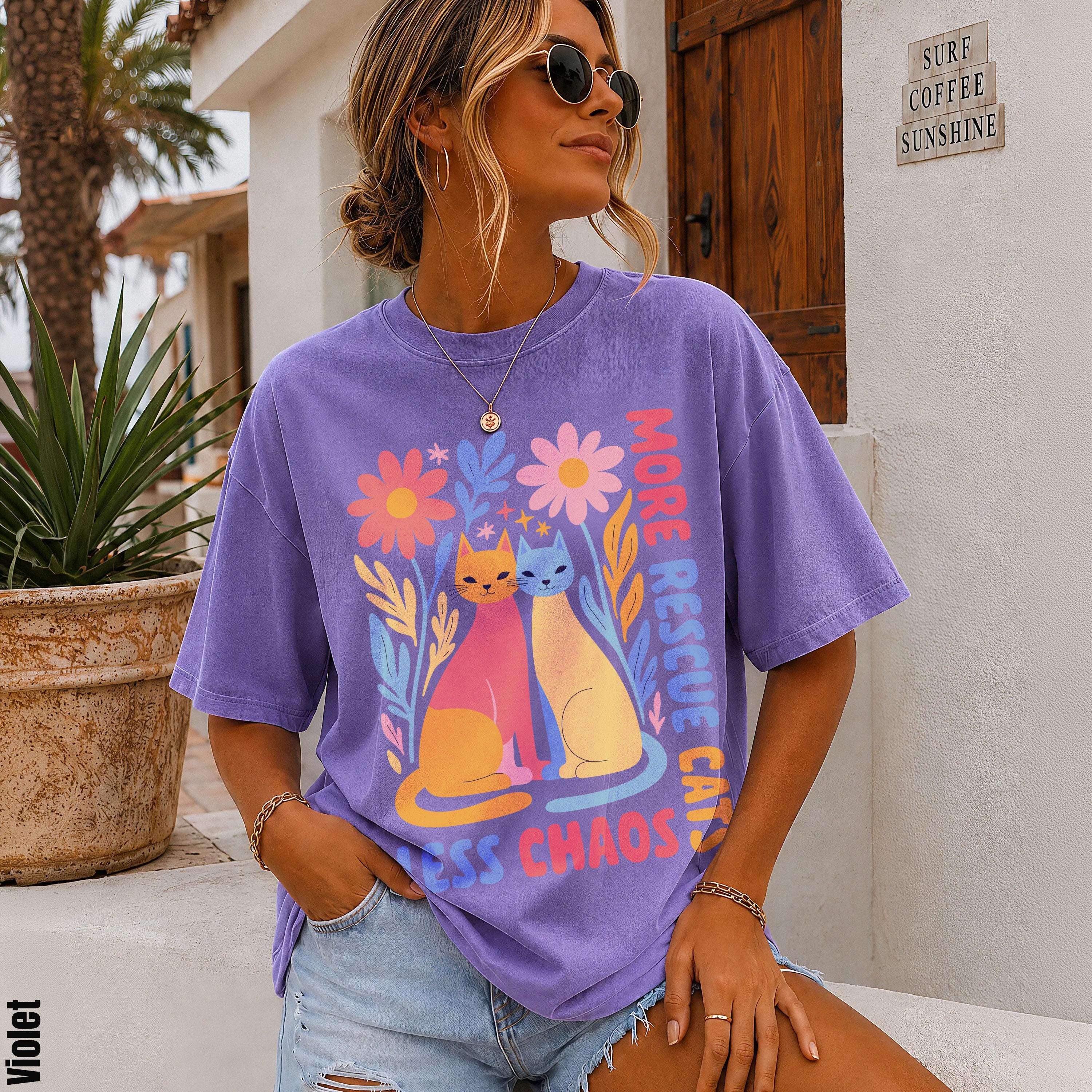 Purple t-shirt with cats, flowers, and "more love less chaos" text.