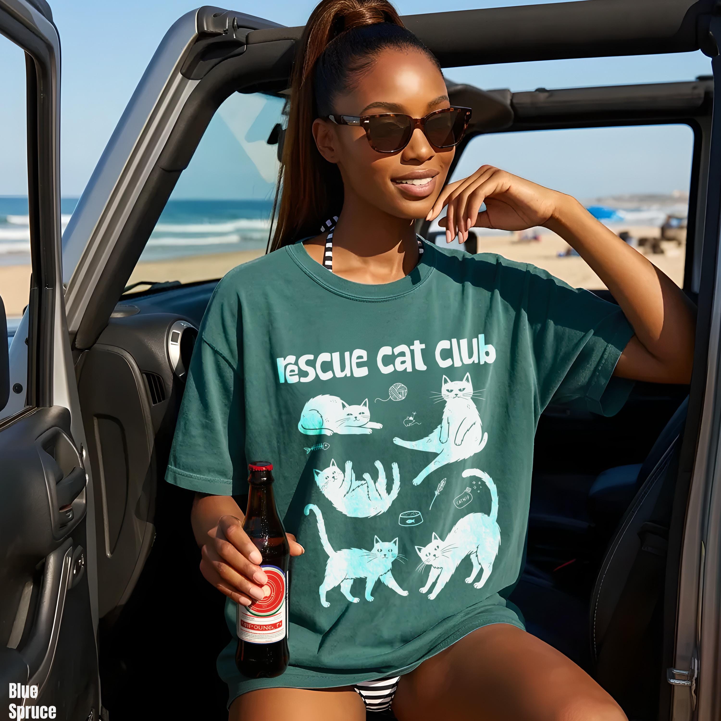 Woman in teal t-shirt with cats, holding a bottle, sitting in a jeep.