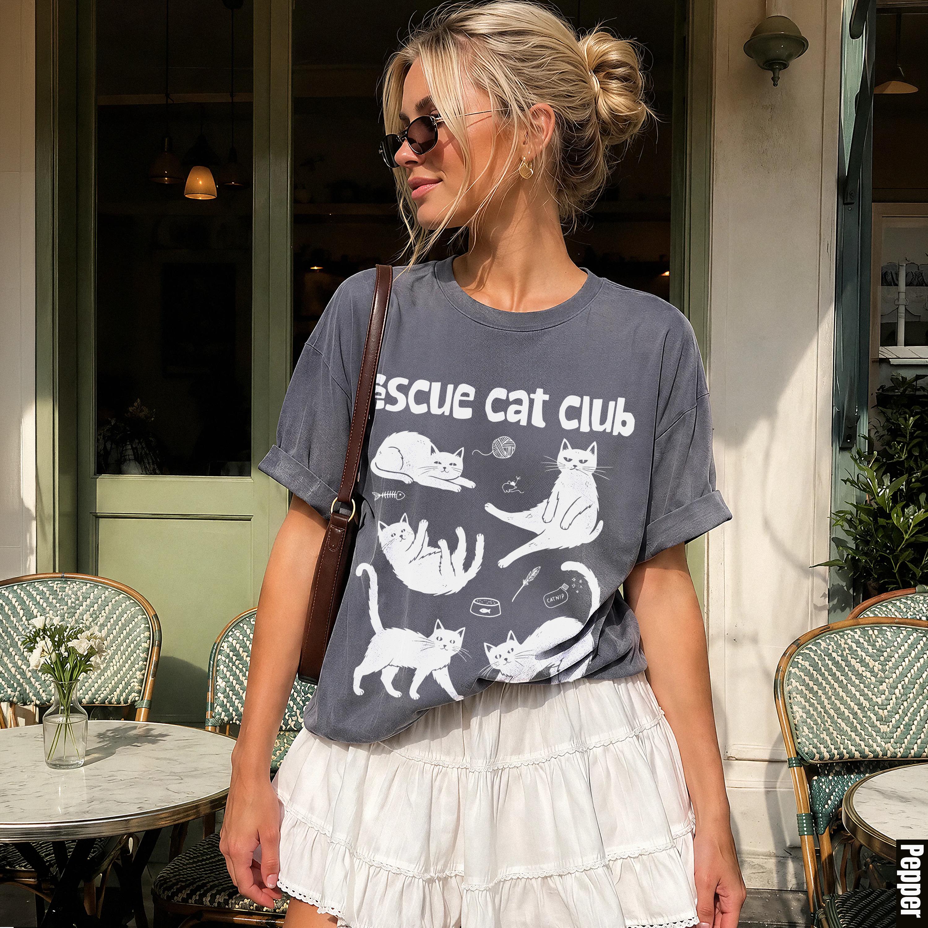 Woman wearing a grey "Rescue Cat Club" t-shirt and white skirt.
