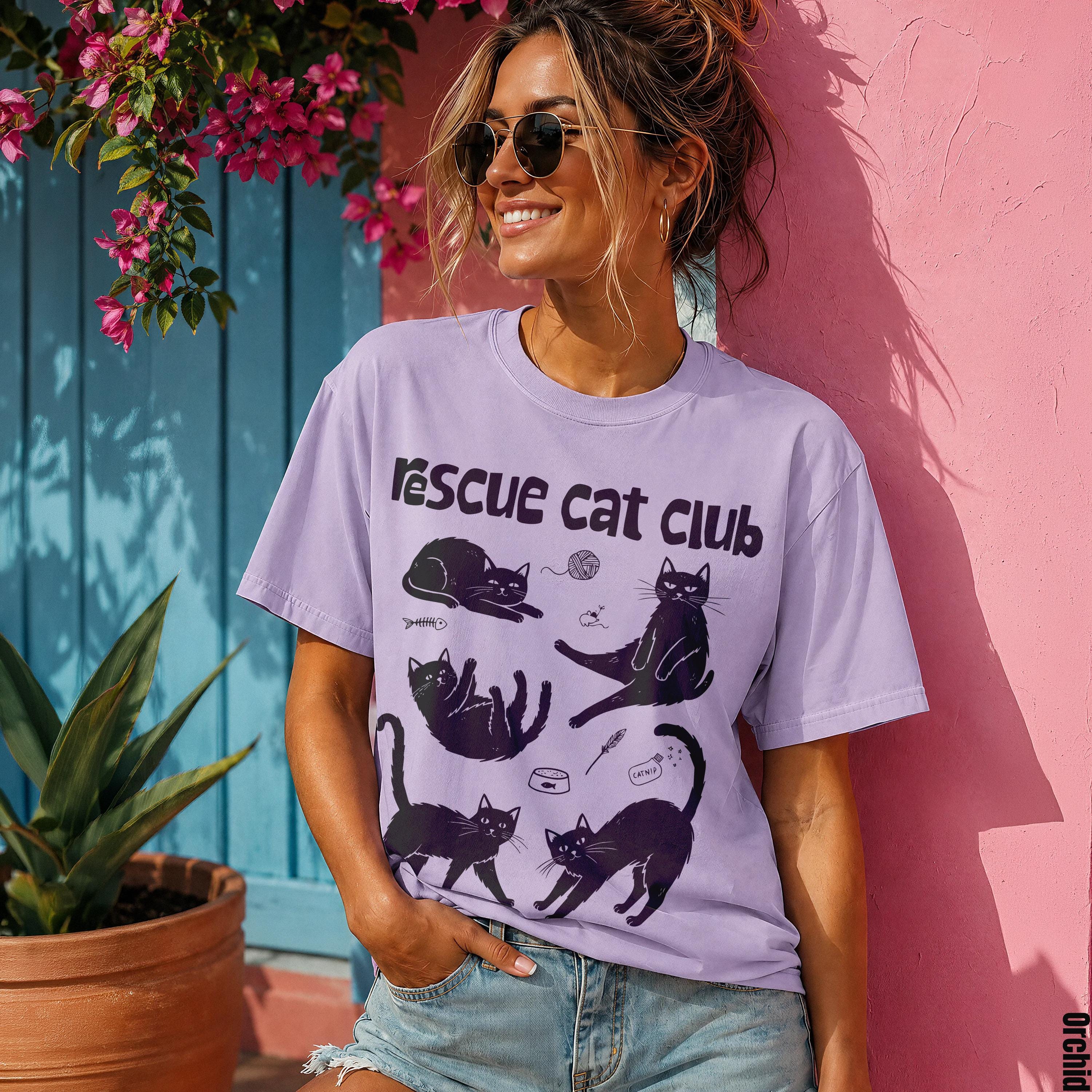Woman wearing a purple t-shirt with black cat illustrations and the text "rescue cat club".