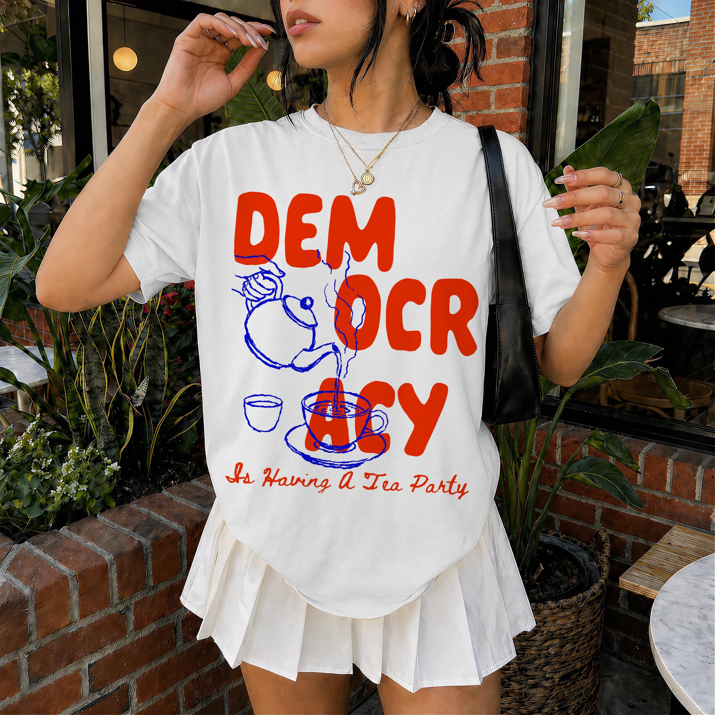 White t-shirt with red text "DEMOCRACY Is Having A Tea Party" and blue tea pouring illustration.