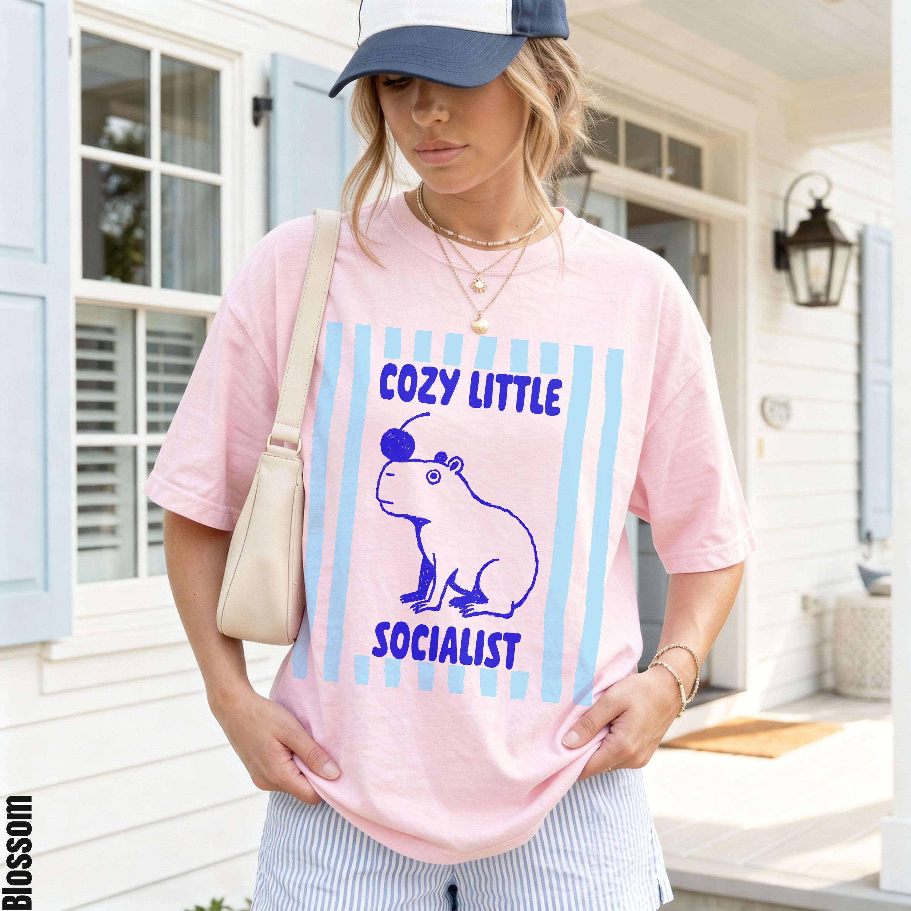 Pink t-shirt with blue capybara graphic and text "COZY LITTLE SOCIALIST".